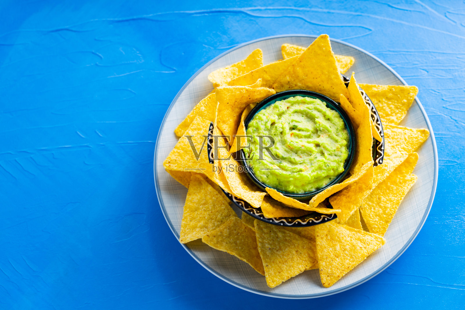 蓝色背景的墨西哥玉米片和鳄梨酱。鳄梨色拉酱配玉米片。副本的空间。俯视图照片摄影图片