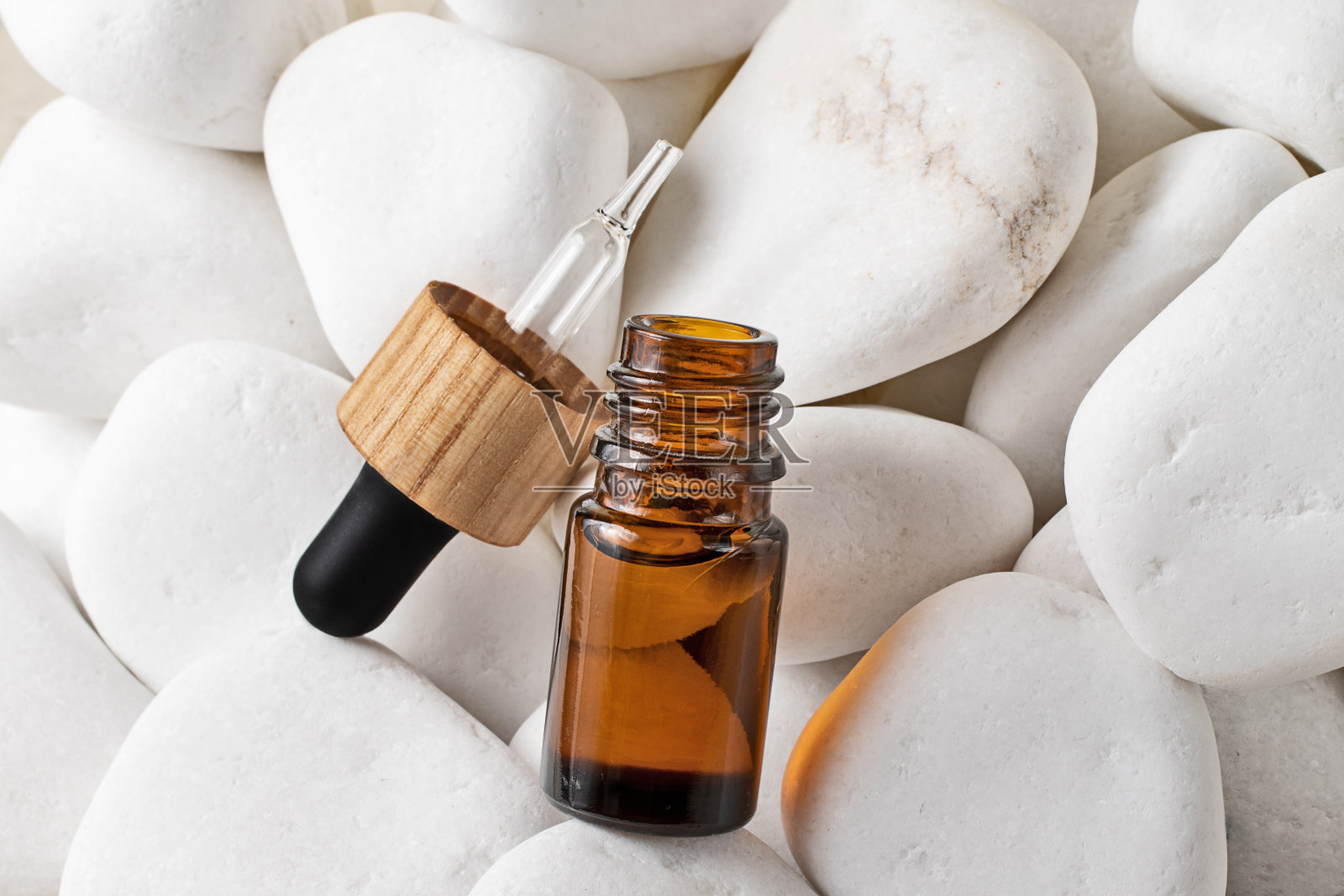 白色的石头上放着一个化妆用的玻璃瓶，带有滴管和打开的盖子。包装采用天然材料-木材和玻璃，化妆品零浪费的概念。模型与复制空间。照片摄影图片