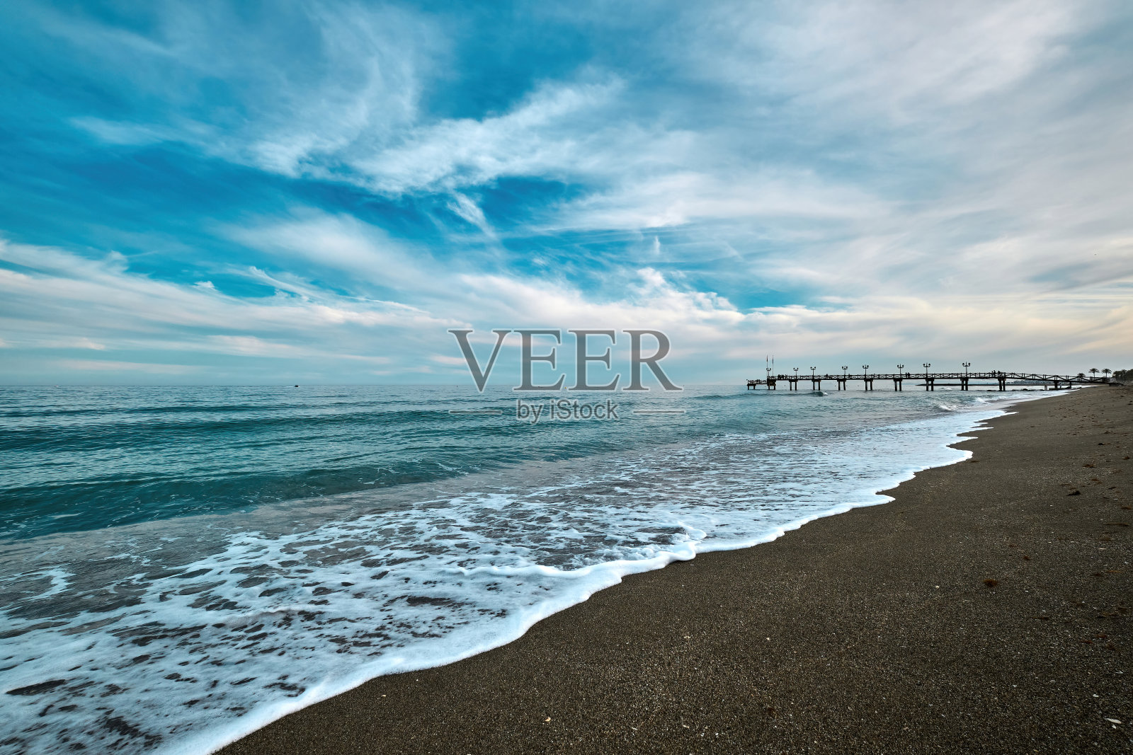 在西班牙度假城市马贝拉的太阳海岸上的沙滩和木制码头。日落和海浪照片摄影图片