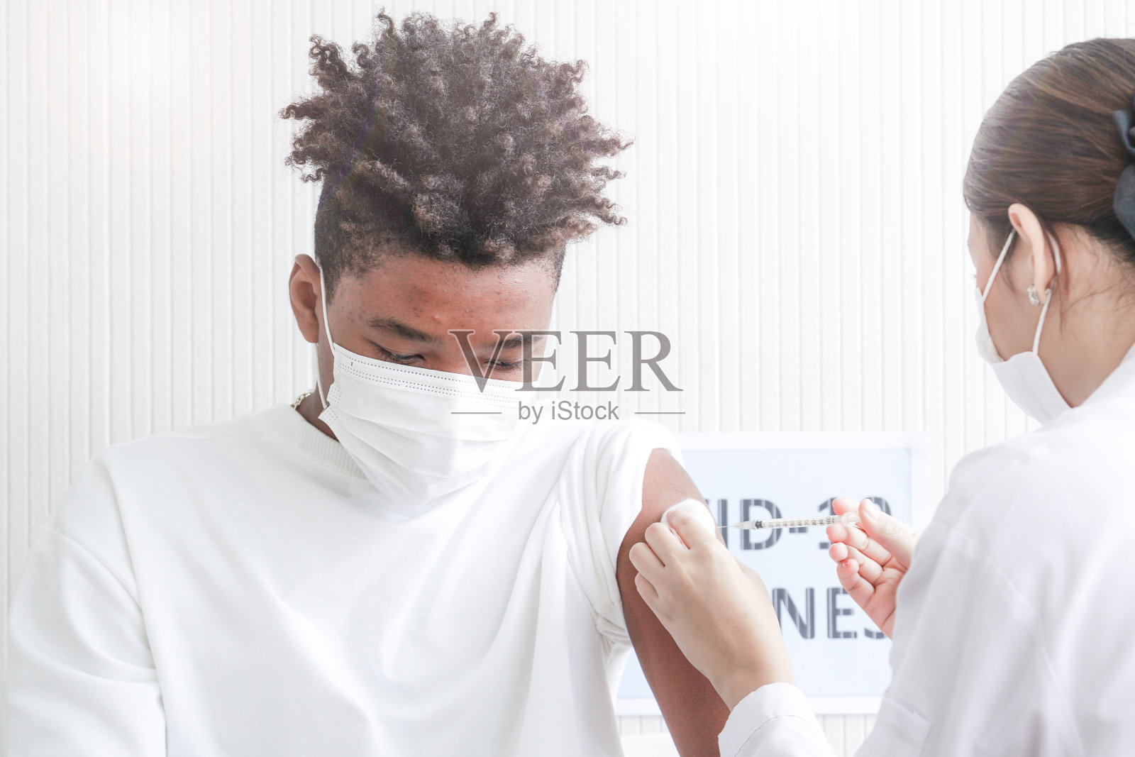 非裔美国人在诊所或医院注射冠状病毒疫苗时，与手护士一起注射疫苗以获得免疫保护病毒的肖像。戴着防护口罩的青少年。照片摄影图片