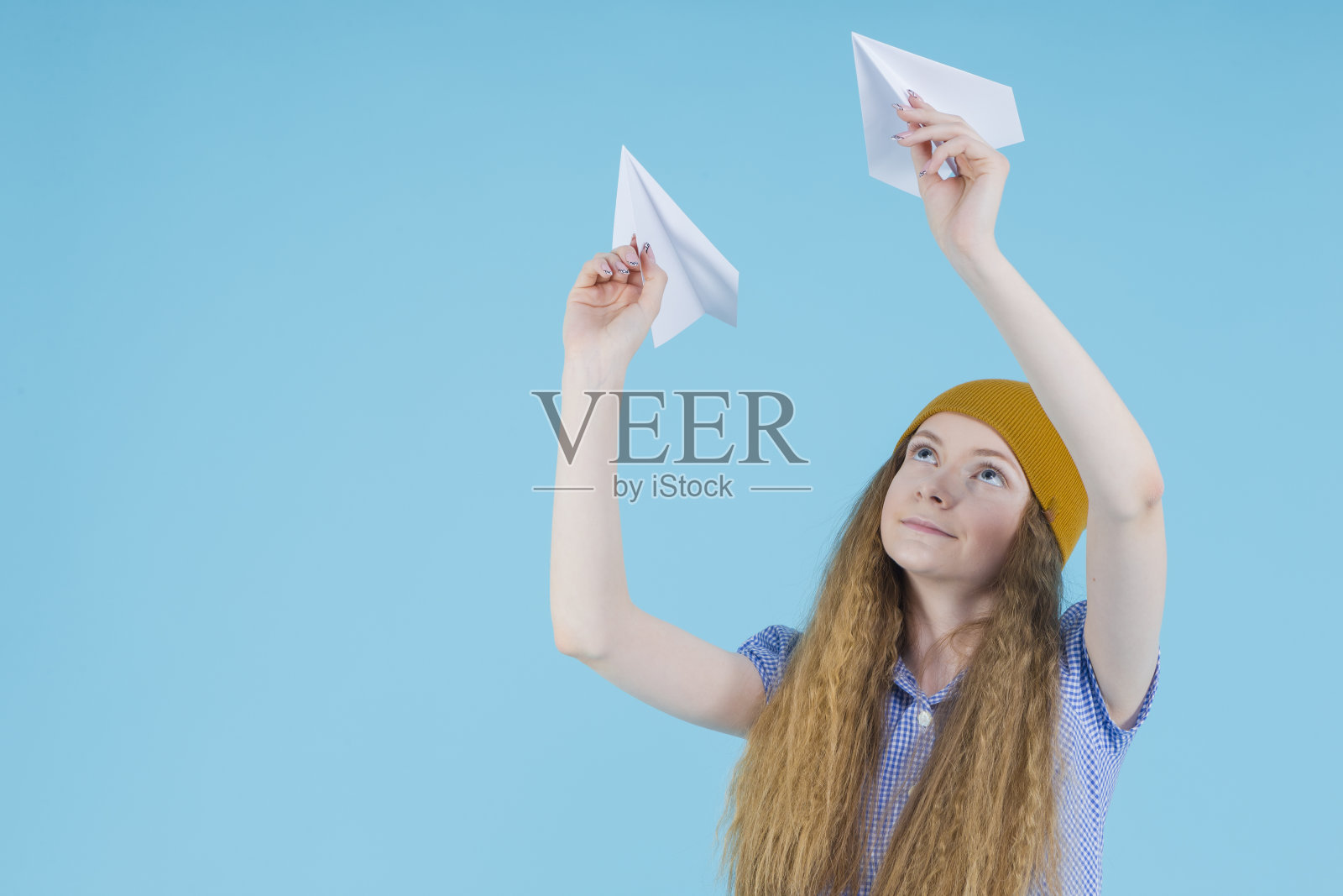 穿蓝色格子裙、戴帽子的金发少女放飞纸飞机照片摄影图片