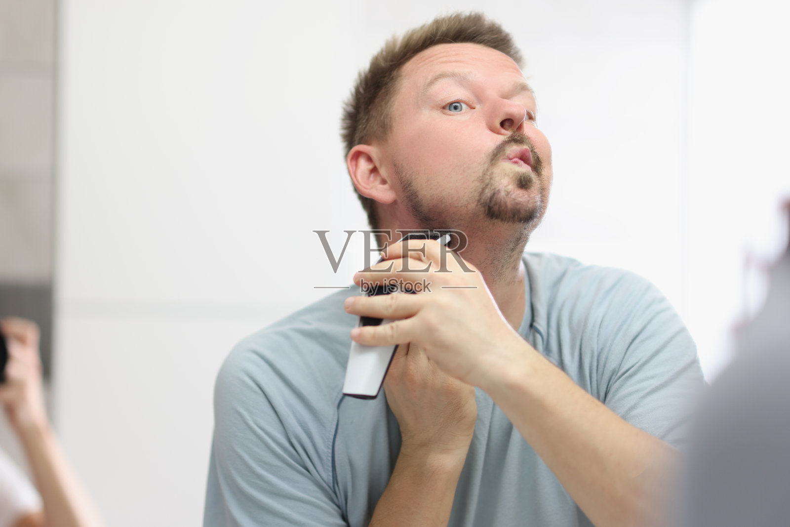 一名年轻人在浴室的镜子前用剃须刀刮胡子照片摄影图片