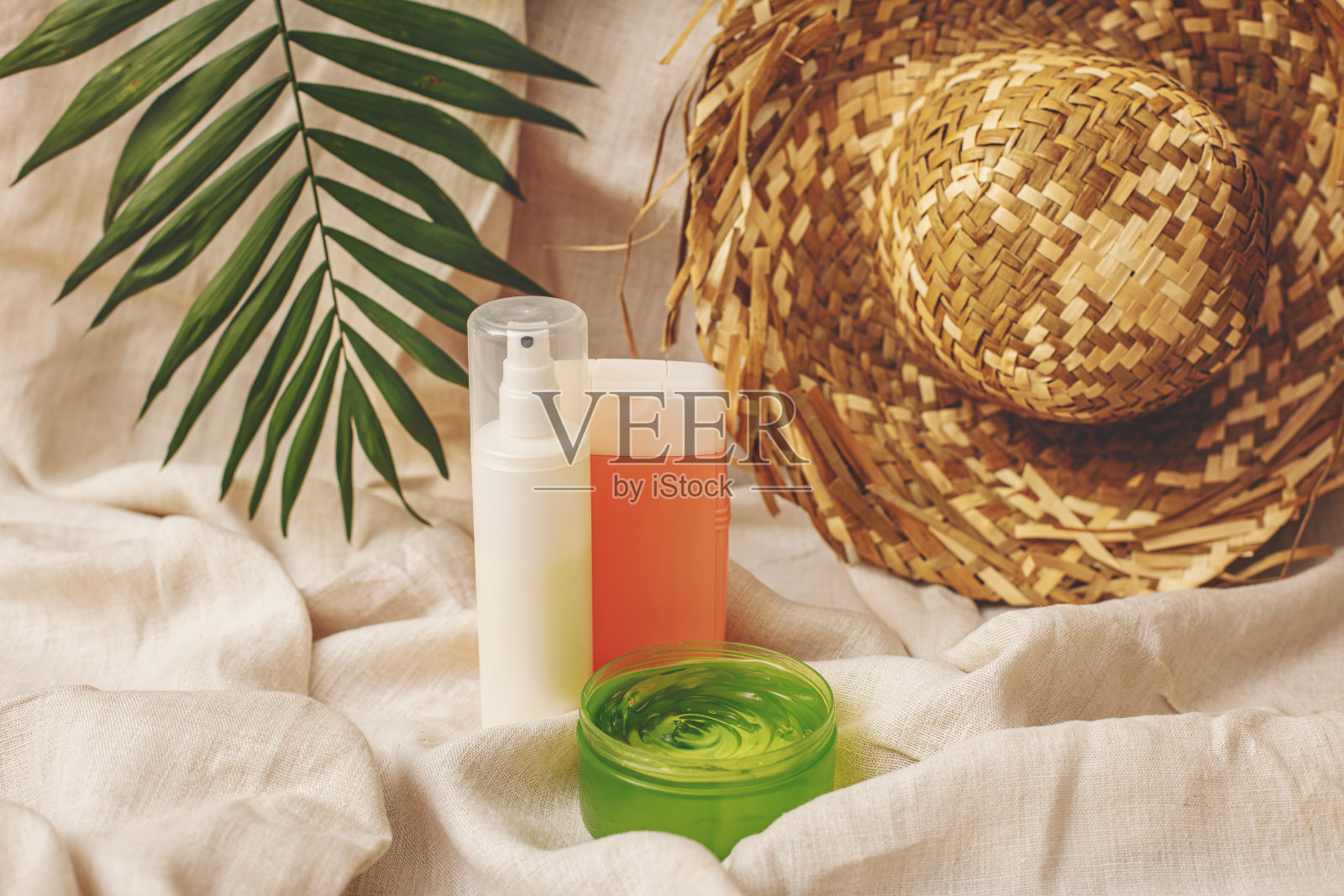 夏季化妆品面霜和凝胶与一顶帽子和棕榈叶在亚麻织物的背景照片摄影图片