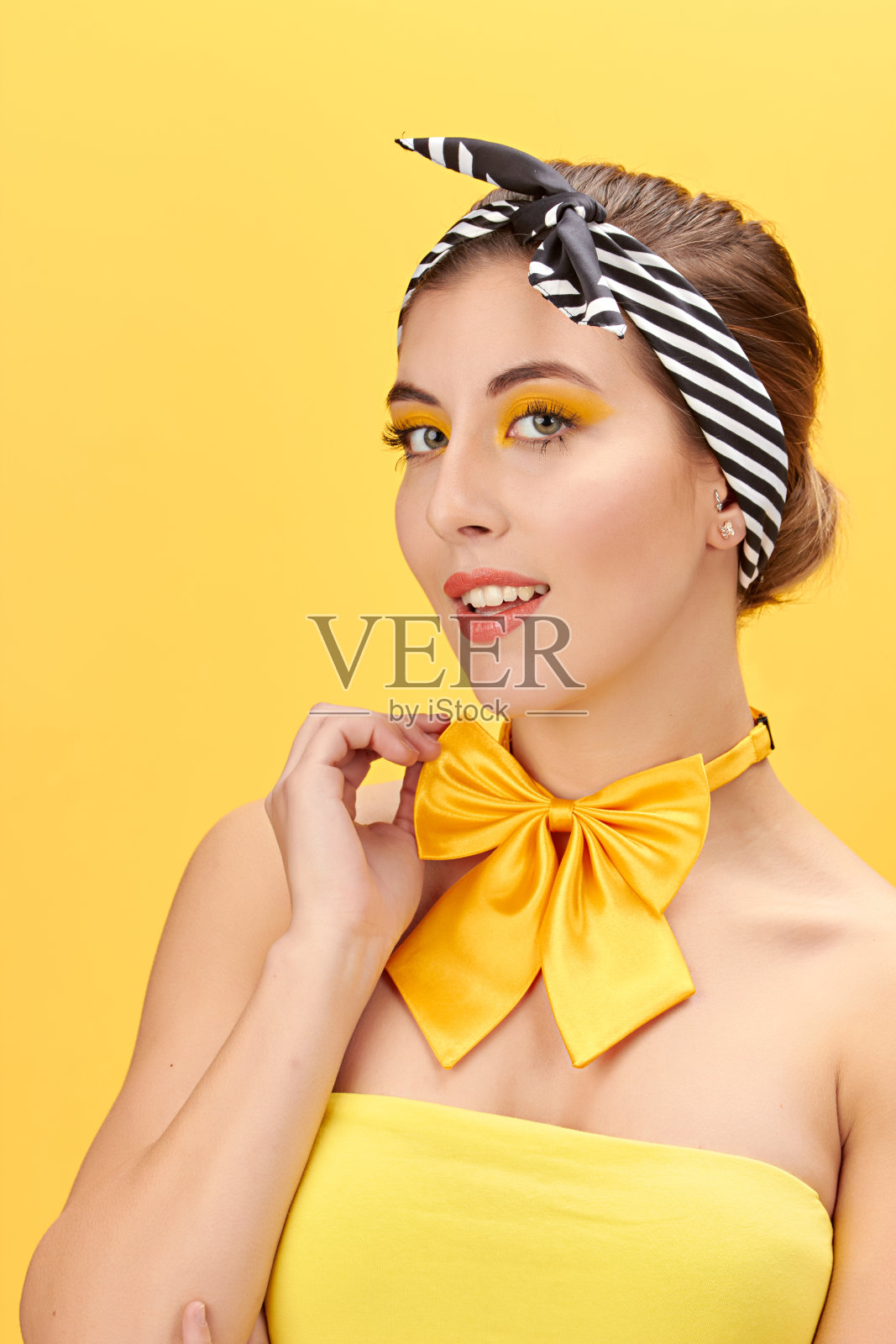 漂亮的女孩，黄色的t恤，黄色的领结，黑色的头巾和红色的嘴唇，黄色的背景。照片摄影图片