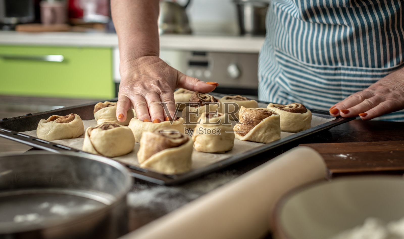 在烘烤之前，妇女的手轻轻地把生肉桂面包放在烤盘上。自制烘焙的烹饪工艺概念照片摄影图片
