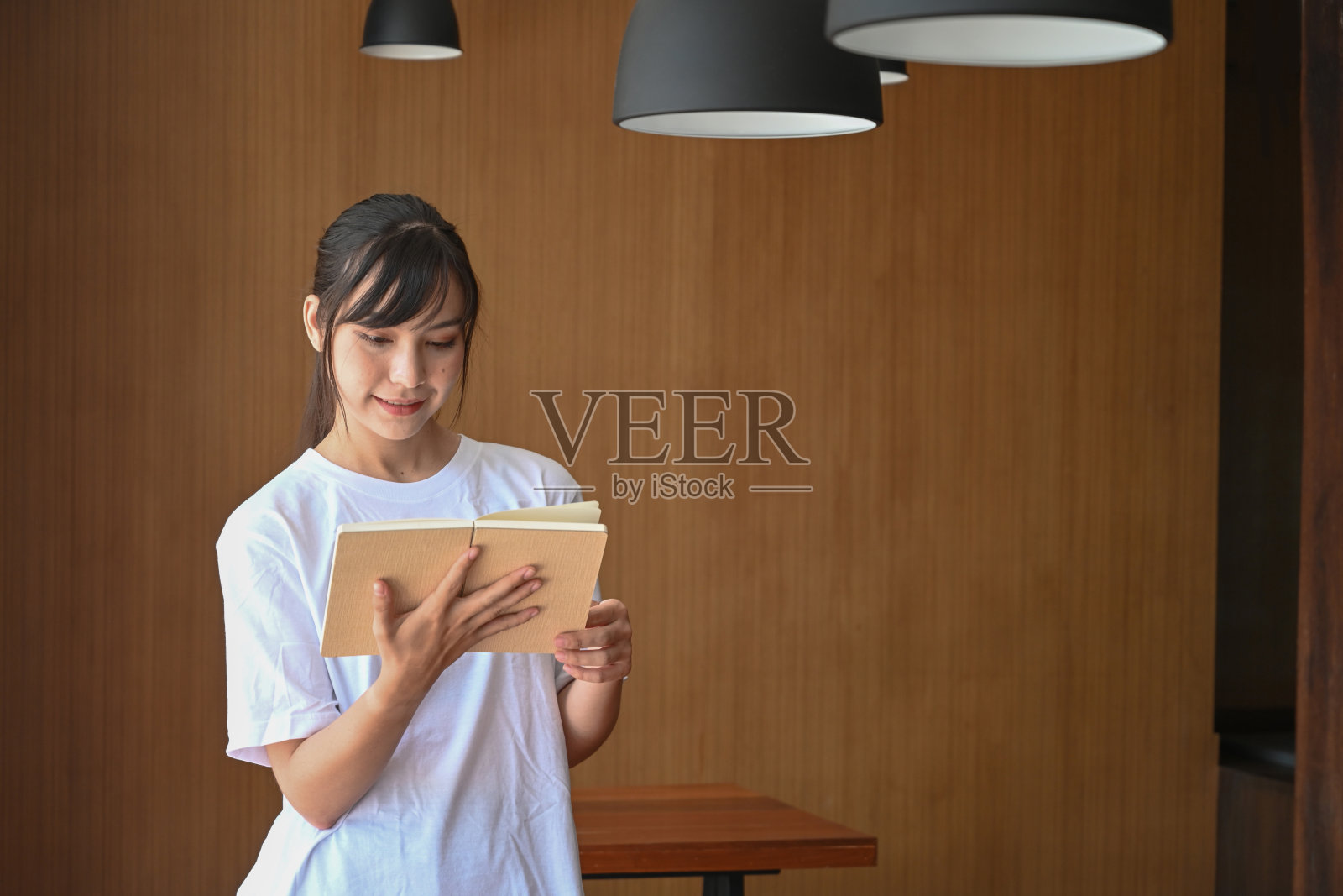 微笑的年轻女学生在图书馆看书。照片摄影图片