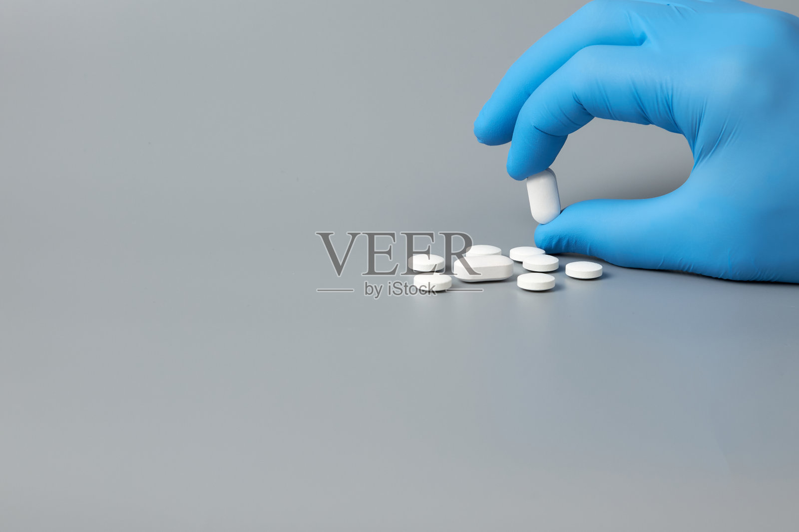 一只戴着手套的手拿着灰色背景上的白色药丸照片摄影图片