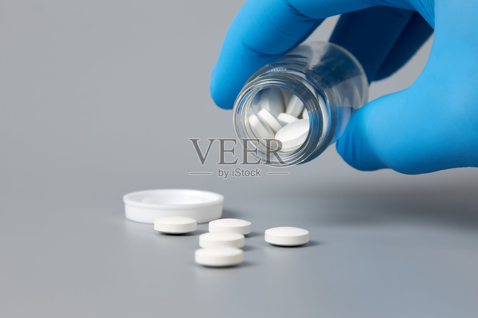 一只戴着蓝色手套的手把药丸倒在灰色的表面上。照片摄影图片