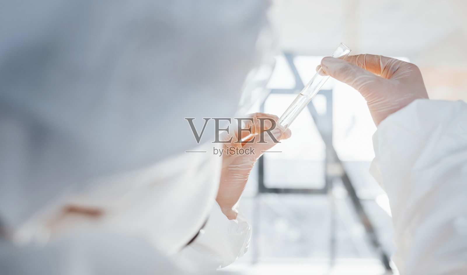 手里拿着试管。女博士科学家穿着实验服，戴着防护眼镜和面罩站在室内照片摄影图片