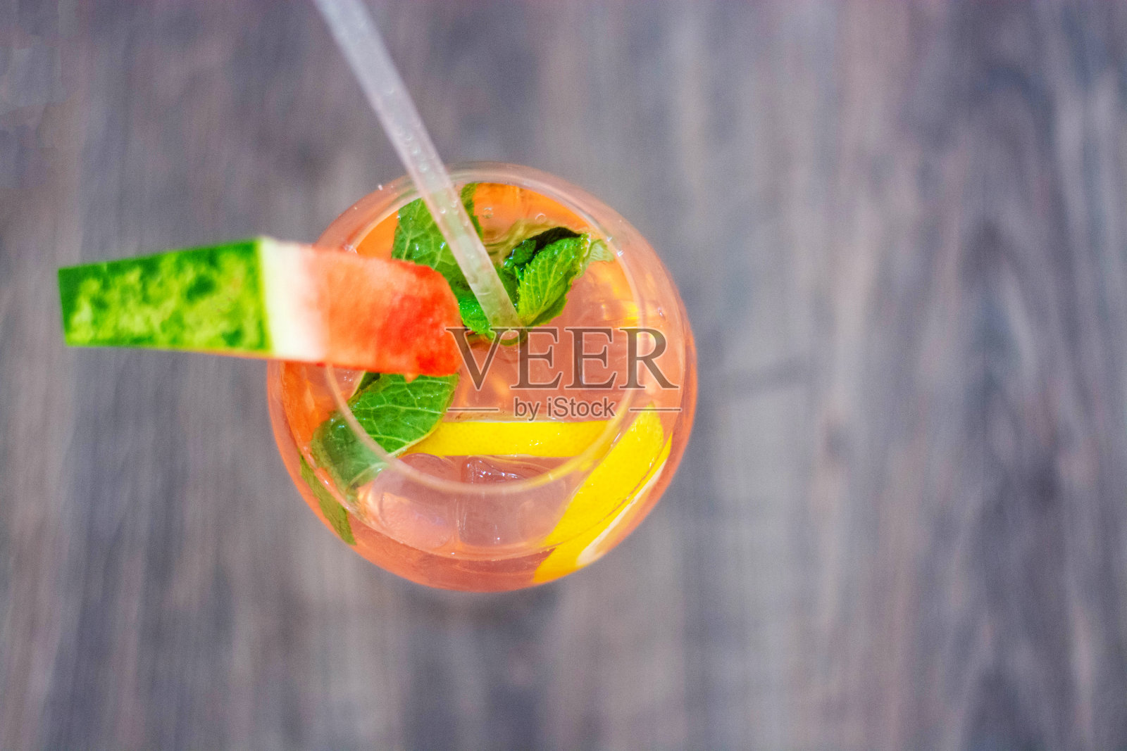 粉红莫吉托鸡尾酒，薄荷，柠檬片和冰块放在木桌上。用一片西瓜装饰。文本空间。照片摄影图片