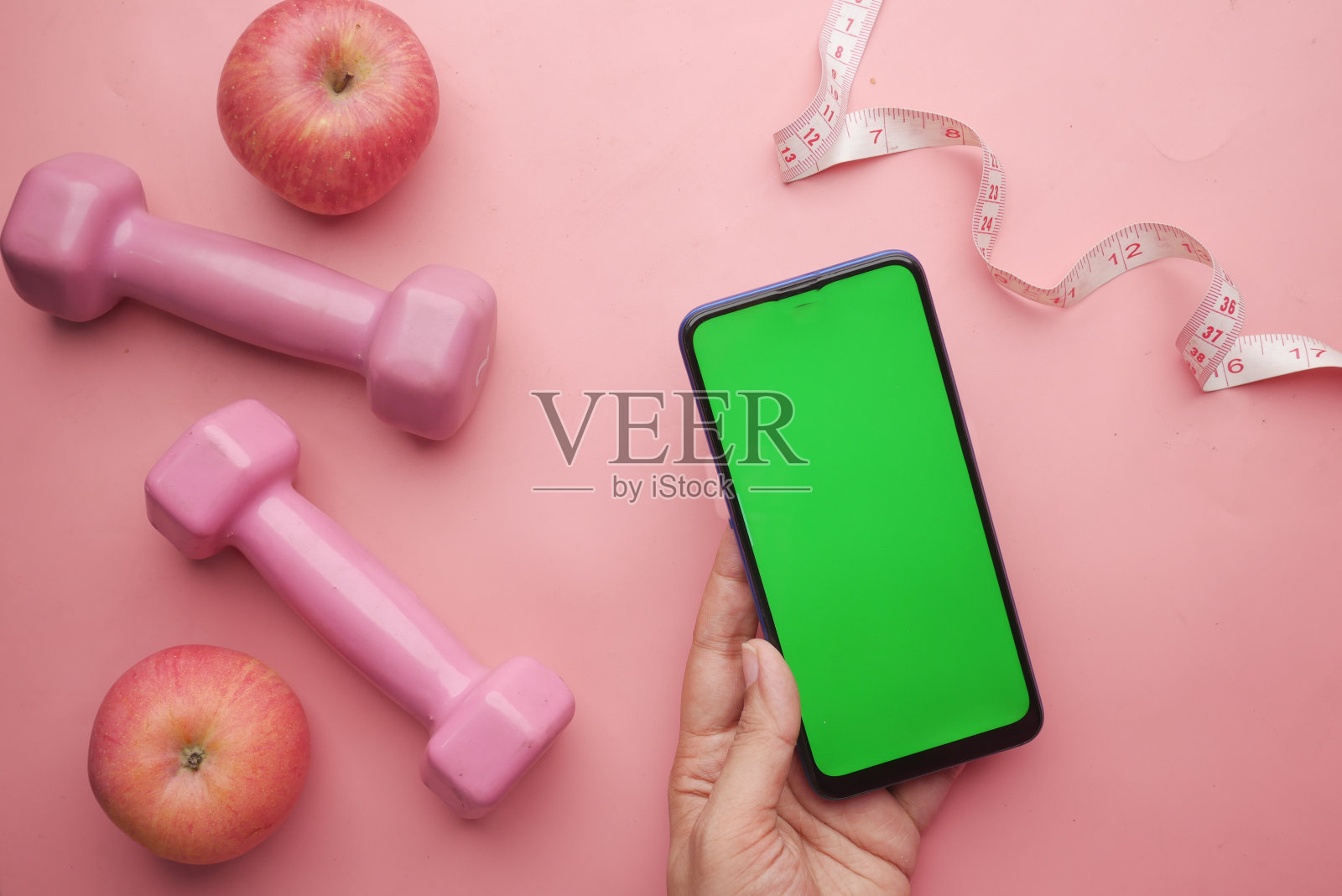 女人手里拿着智能手机的哑铃和苹果在粉红色照片摄影图片