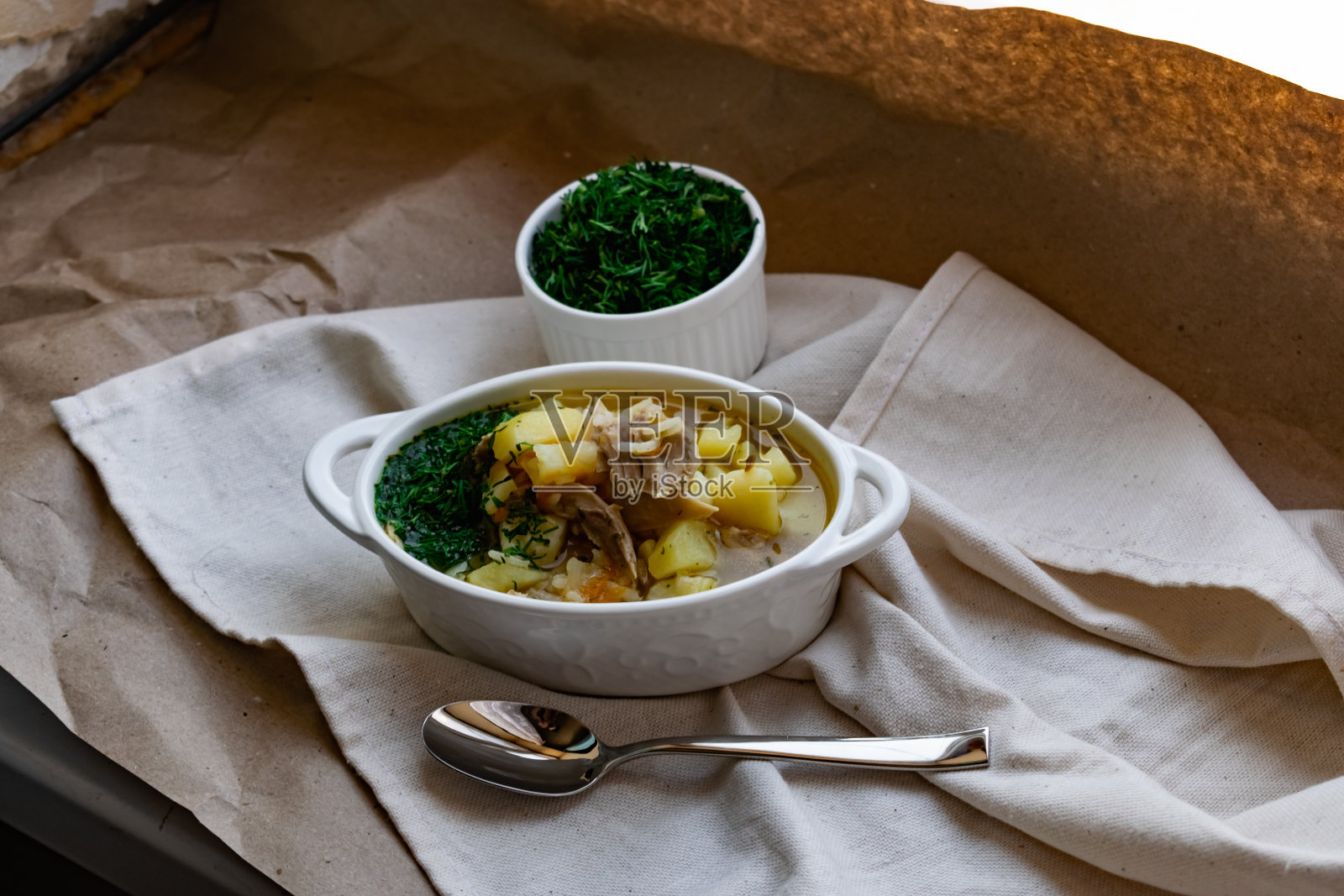 热鸡汤，土豆，肉和新鲜的莳萝在有趣的陶瓷菜肴，在羊皮纸和纺织品照片摄影图片
