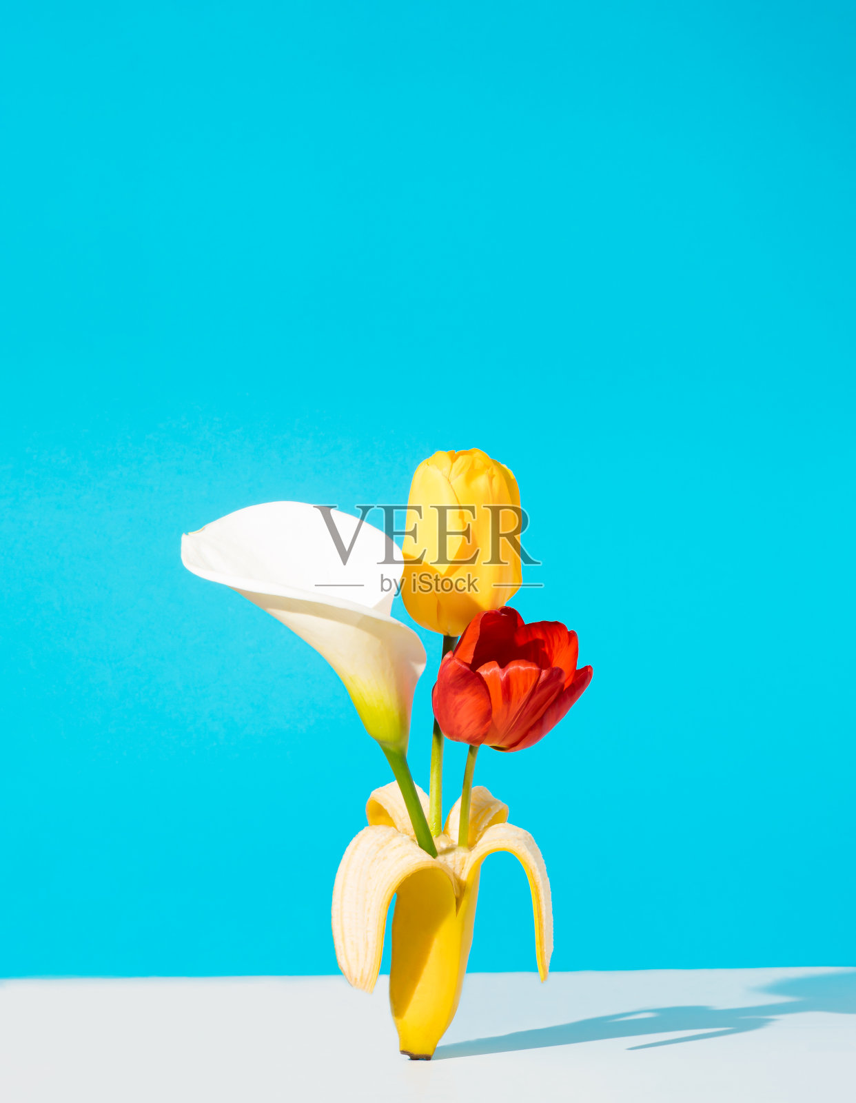 创意的布局，香蕉水果和盛开的春天的花朵在蓝色的背景。最小的复古风格。照片摄影图片