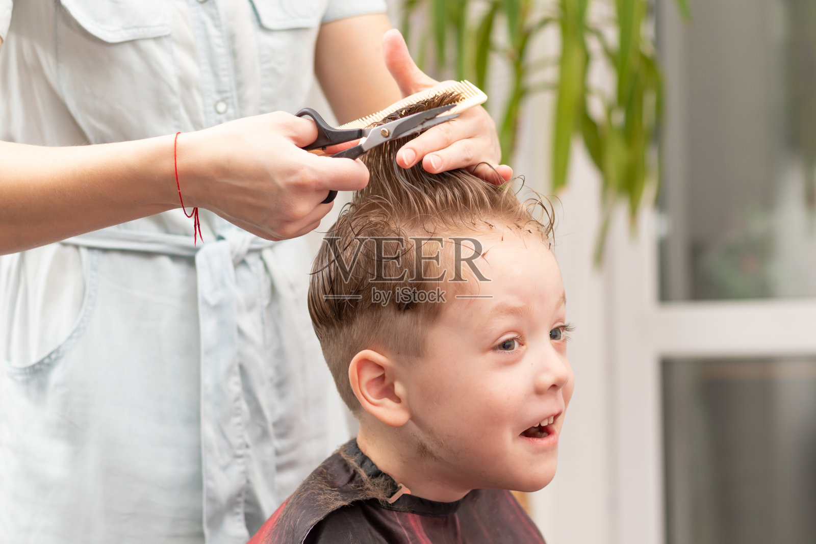 在第二次封锁期间，一位母亲用梳子和剪刀在家里为儿子做了一个时尚的发型。有选择性的重点照片摄影图片