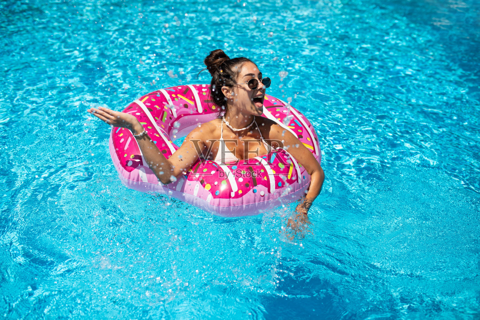 在一个炎热的夏天，一个美丽的女孩在充气甜甜圈上的游泳池里玩得很开心照片摄影图片