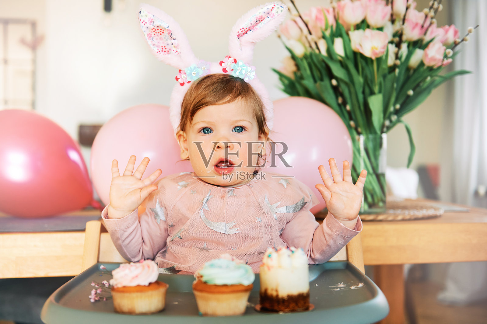 可爱的小女孩的滑稽肖像印象深刻的选择纸杯蛋糕，戴着兔子耳朵，复活节的概念照片摄影图片