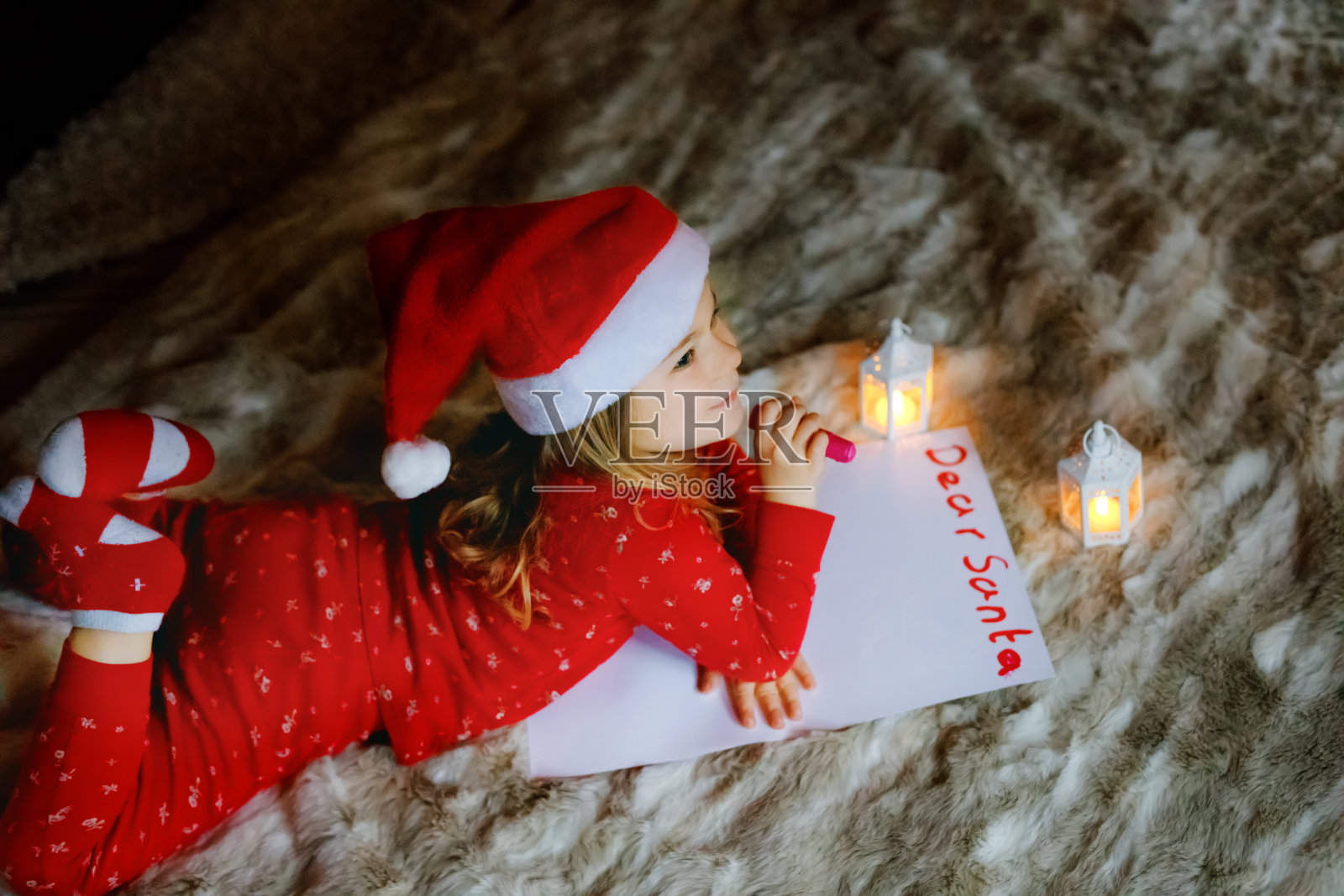 可爱的小女孩躺在圣诞树下的床上，在家给圣诞老人写愿望单。传统的基督教节日。快乐的孩子等待圣诞礼物。照片摄影图片