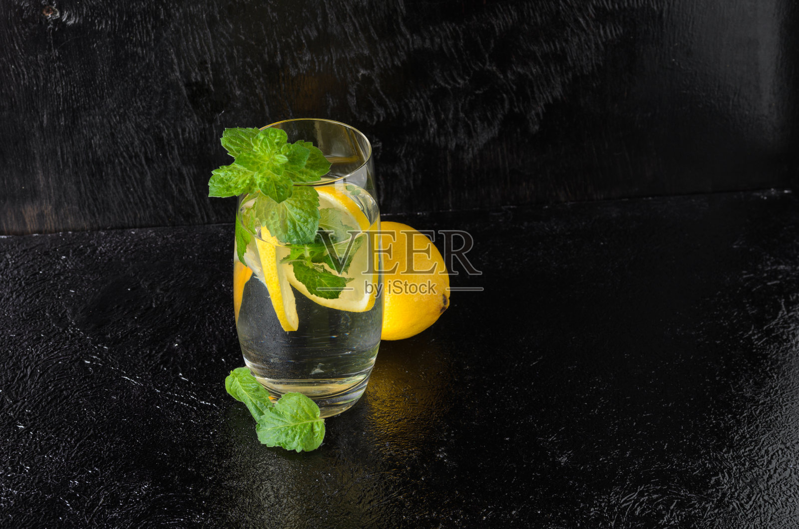 一大杯水加柠檬，薄荷叶。一杯柠檬水在一个黑色纹理的背景。照片摄影图片