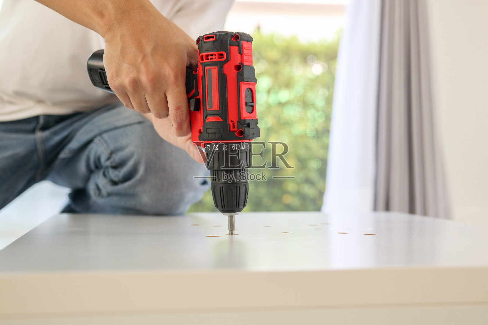 一个人在家里用无绳螺丝刀组装白色桌椅照片摄影图片