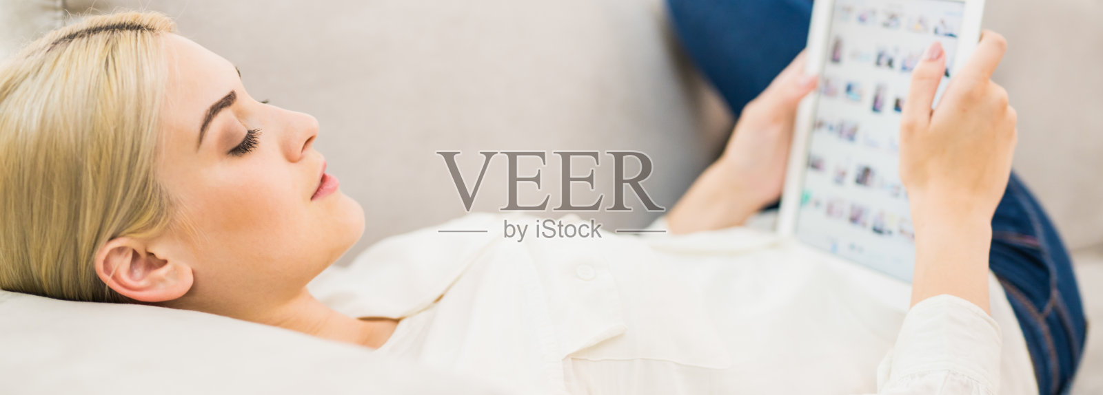 拿着写字板的年轻女子躺在沙发上照片摄影图片