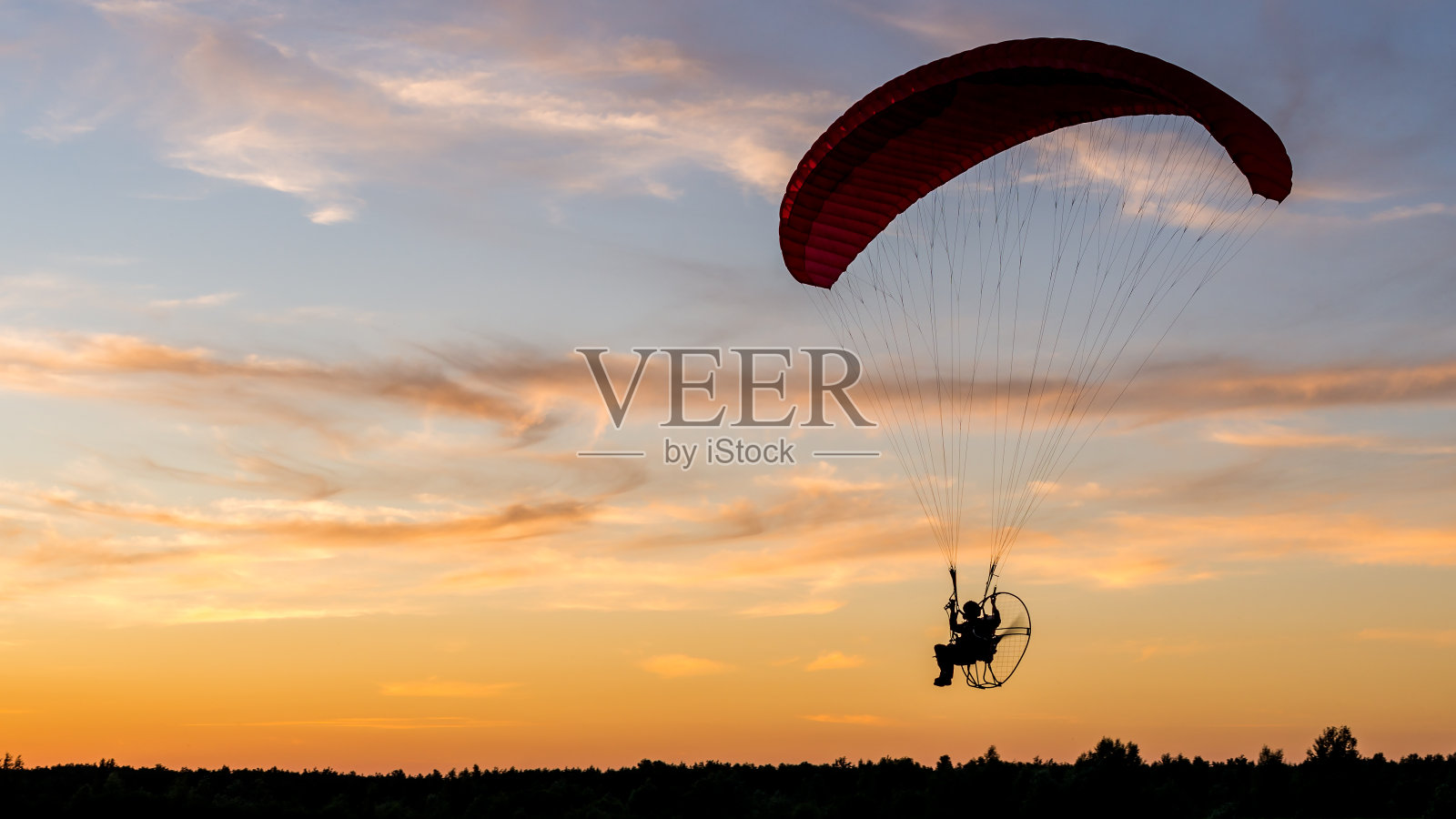 动力滑翔伞飞行员剪影与后置马达(滑翔伞)在日落照片摄影图片