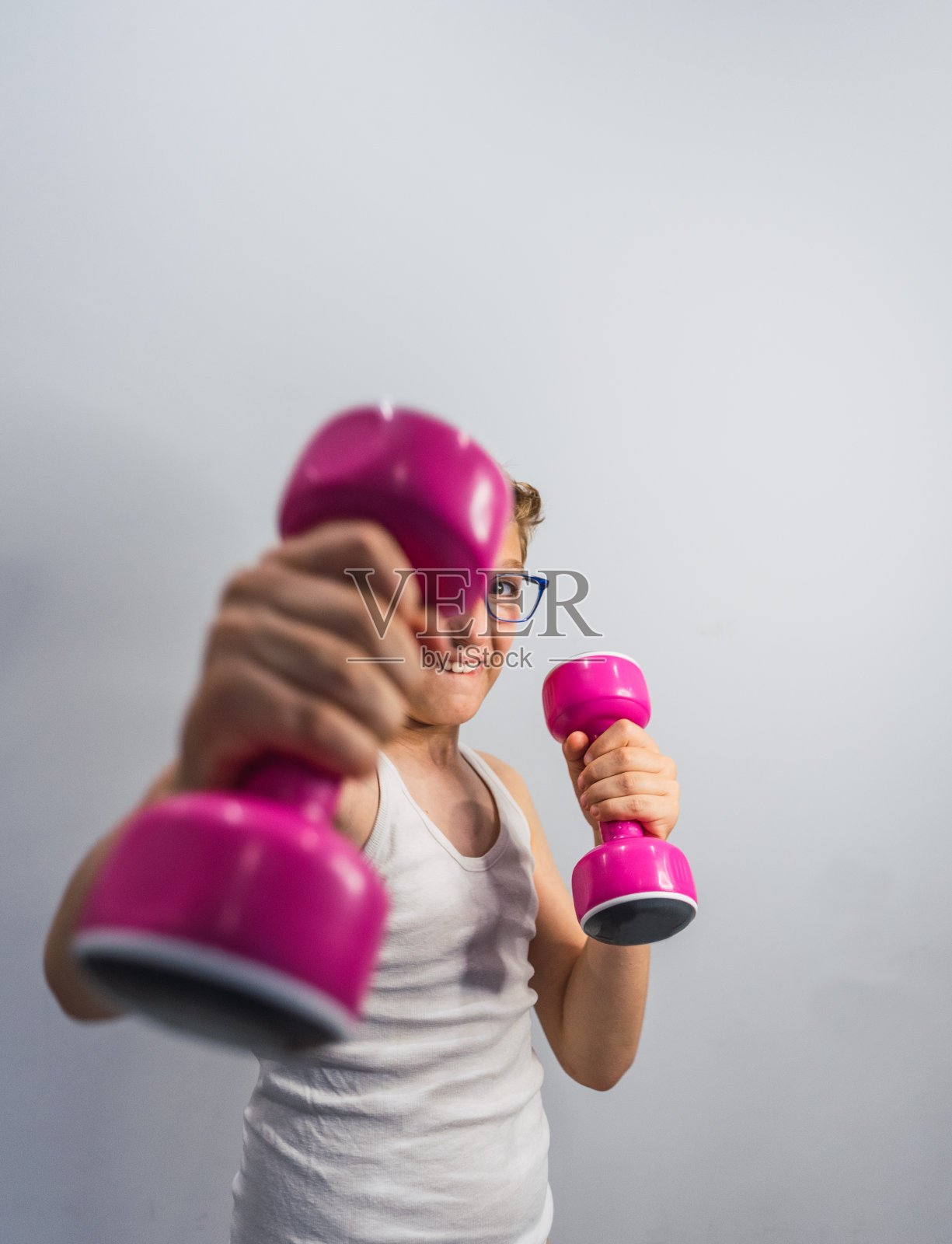 戴眼镜的金发男孩微笑着举着粉色的哑铃照片摄影图片