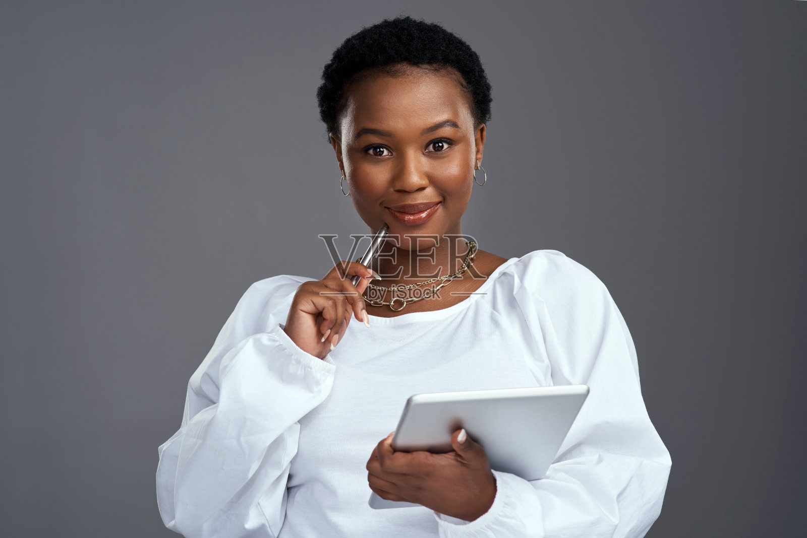 这是一名年轻女子站在灰色背景下使用数码平板电脑的照片照片摄影图片