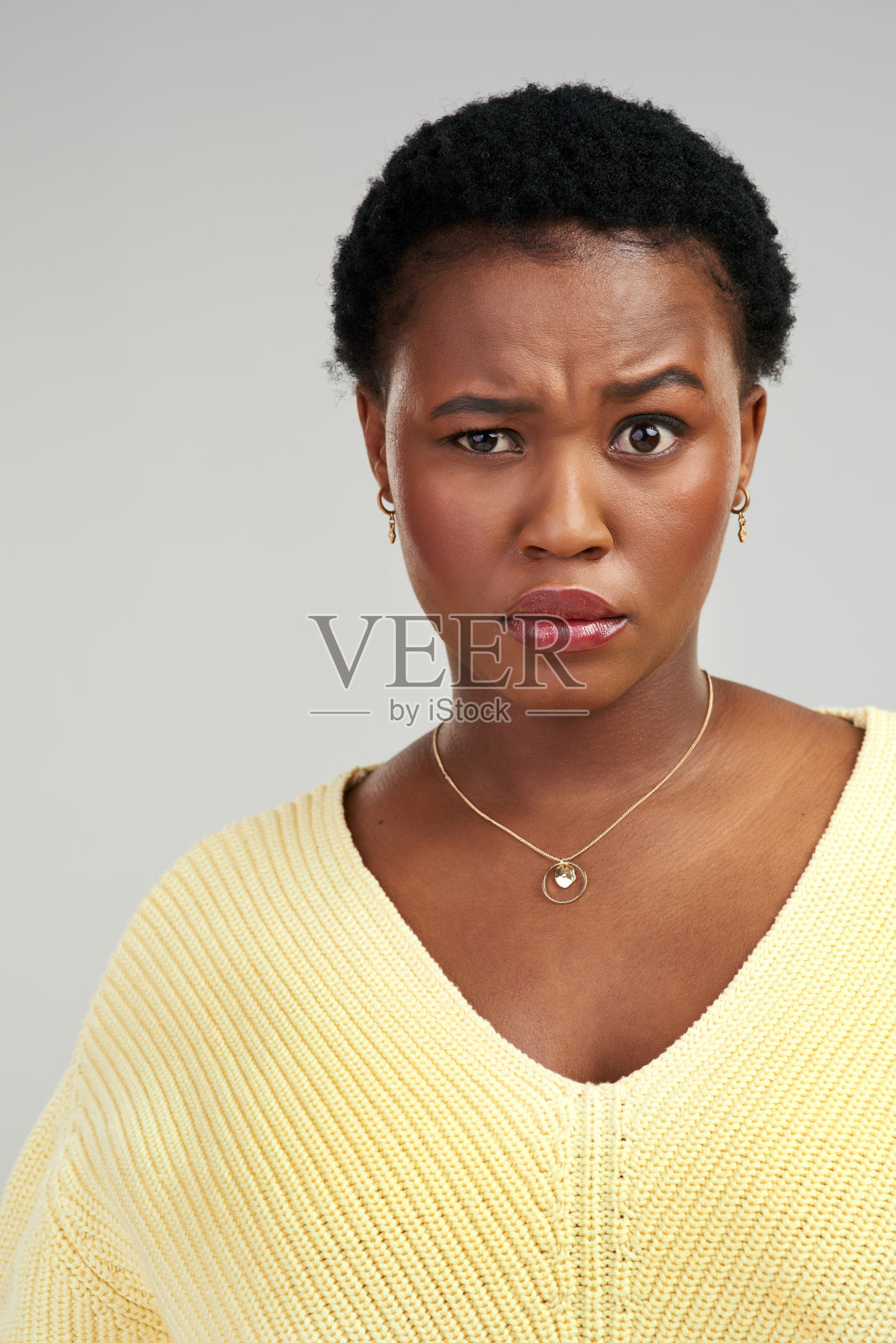 一个年轻女人的照片，皱着眉头，站在一个灰色的背景照片摄影图片