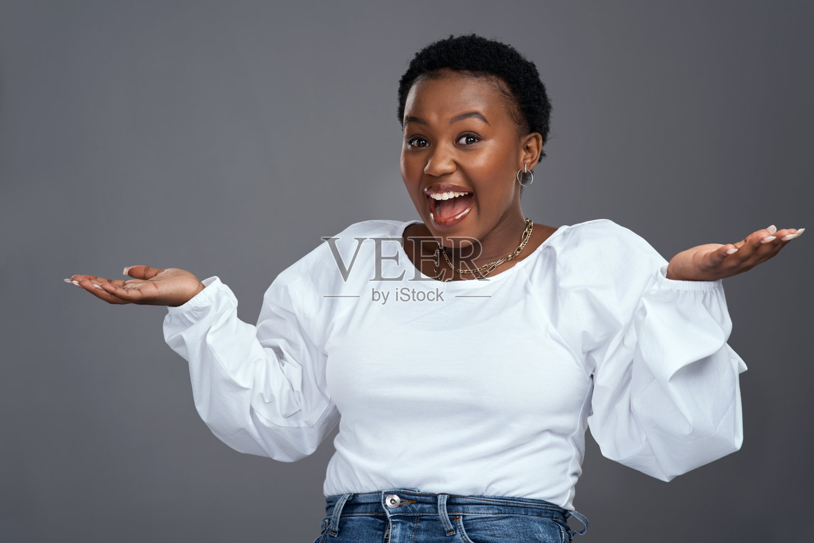 一名年轻女子举起双手，站在灰色背景下照片摄影图片