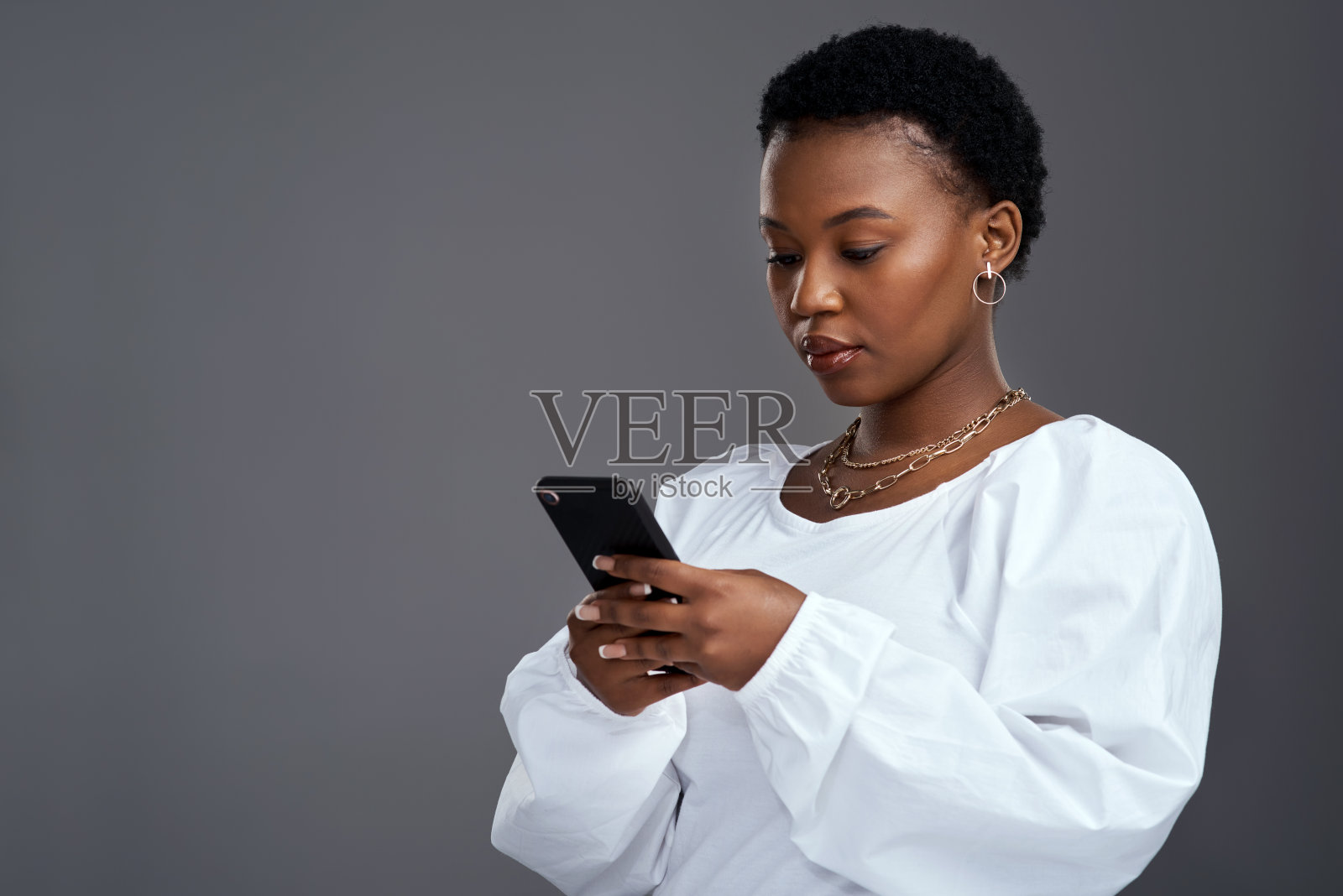 一名年轻女子站在灰色背景下使用手机的照片照片摄影图片