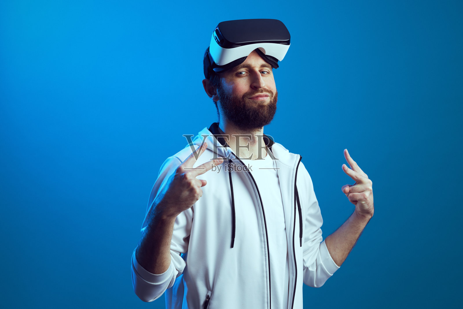 额头戴VR眼镜的男子在蓝色背景下做出和平手势照片摄影图片