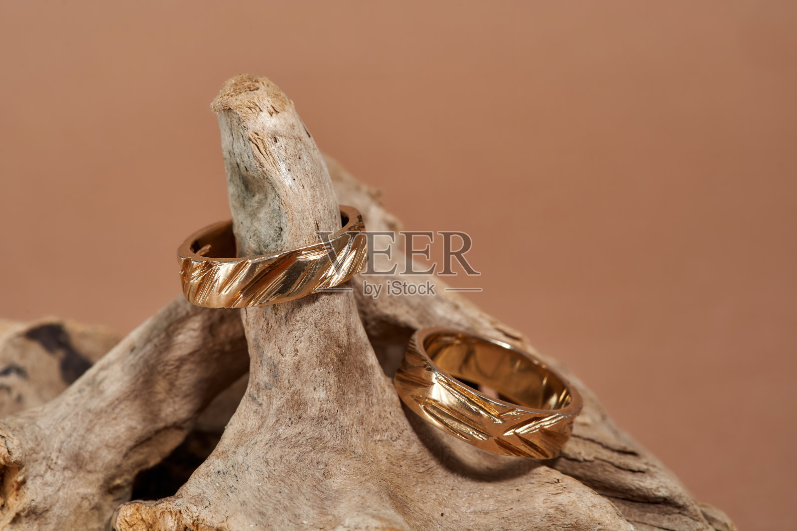 两个漂亮的金戒指的特写，带有凹槽排列在米色背景的木制元素上照片摄影图片