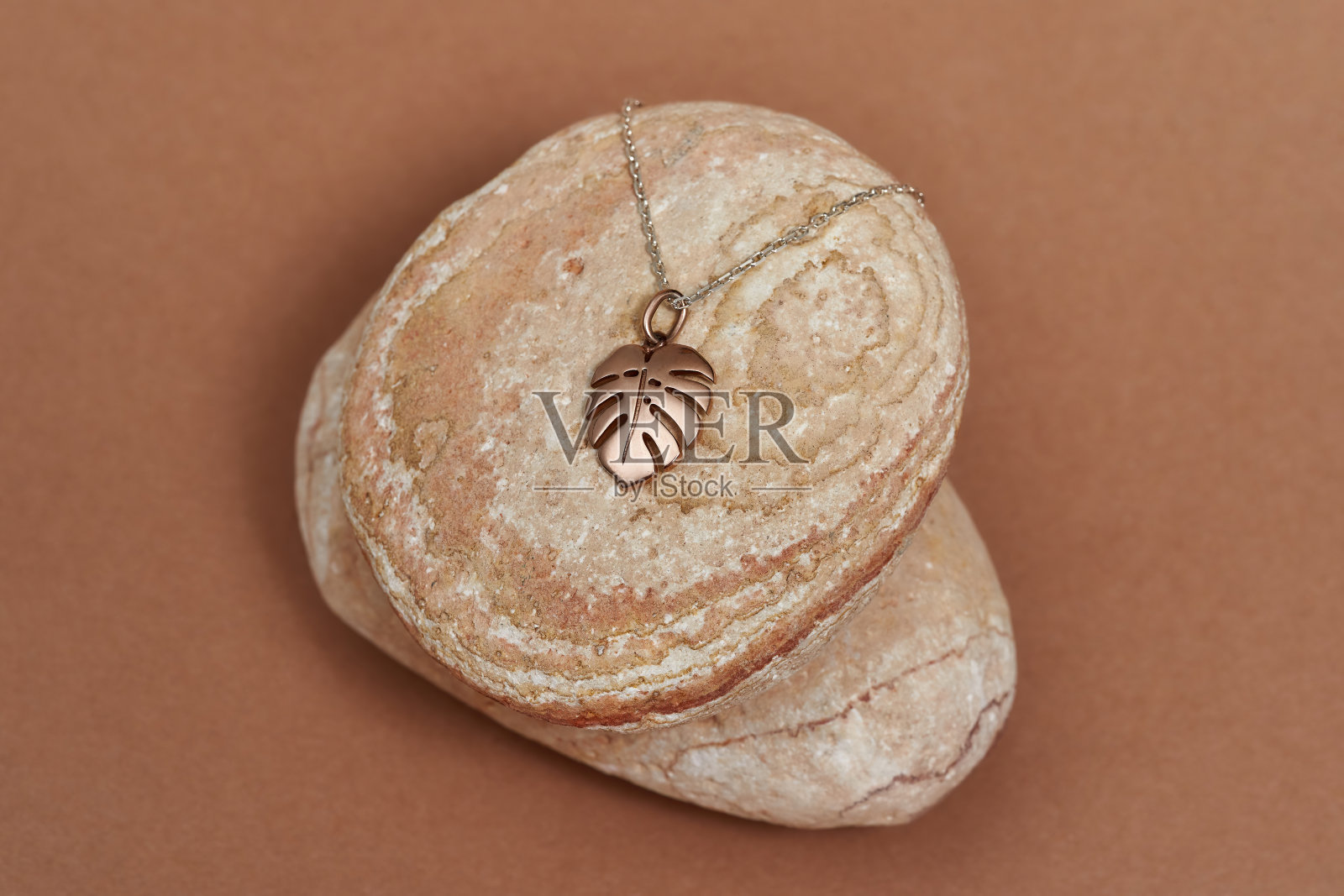 俯视图的黄金链和垂饰在一个怪物的叶子形状的岩石在米色的背景照片摄影图片