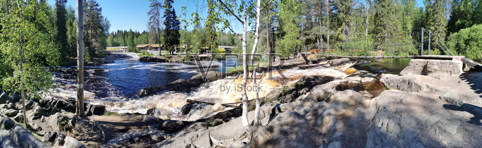在一个晴朗的夏日早晨，卡累利阿托克马约基河上的阿赫温科斯基瀑布风景如画，上面有一座吊桥。照片摄影图片