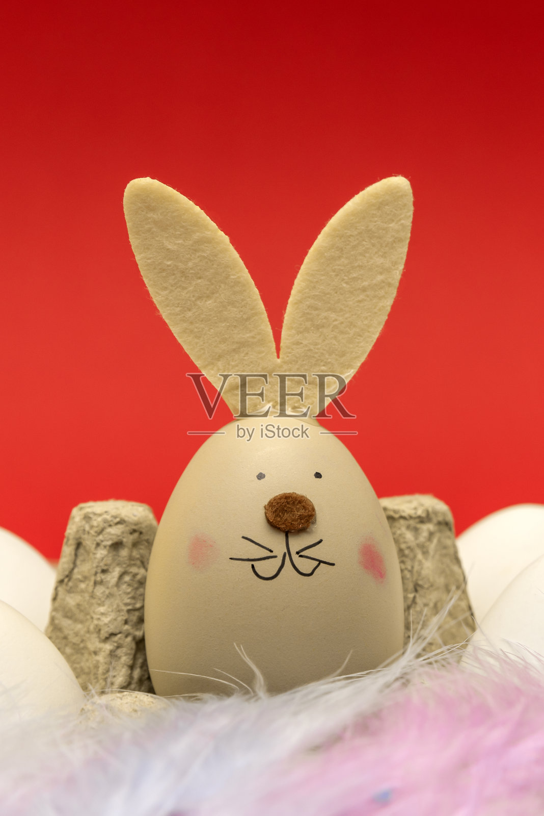 带兔耳朵和口吻的鸡蛋放在环保纸盒里。在红色背景上放置文本。复活节节日快乐概念。极简主义照片摄影图片