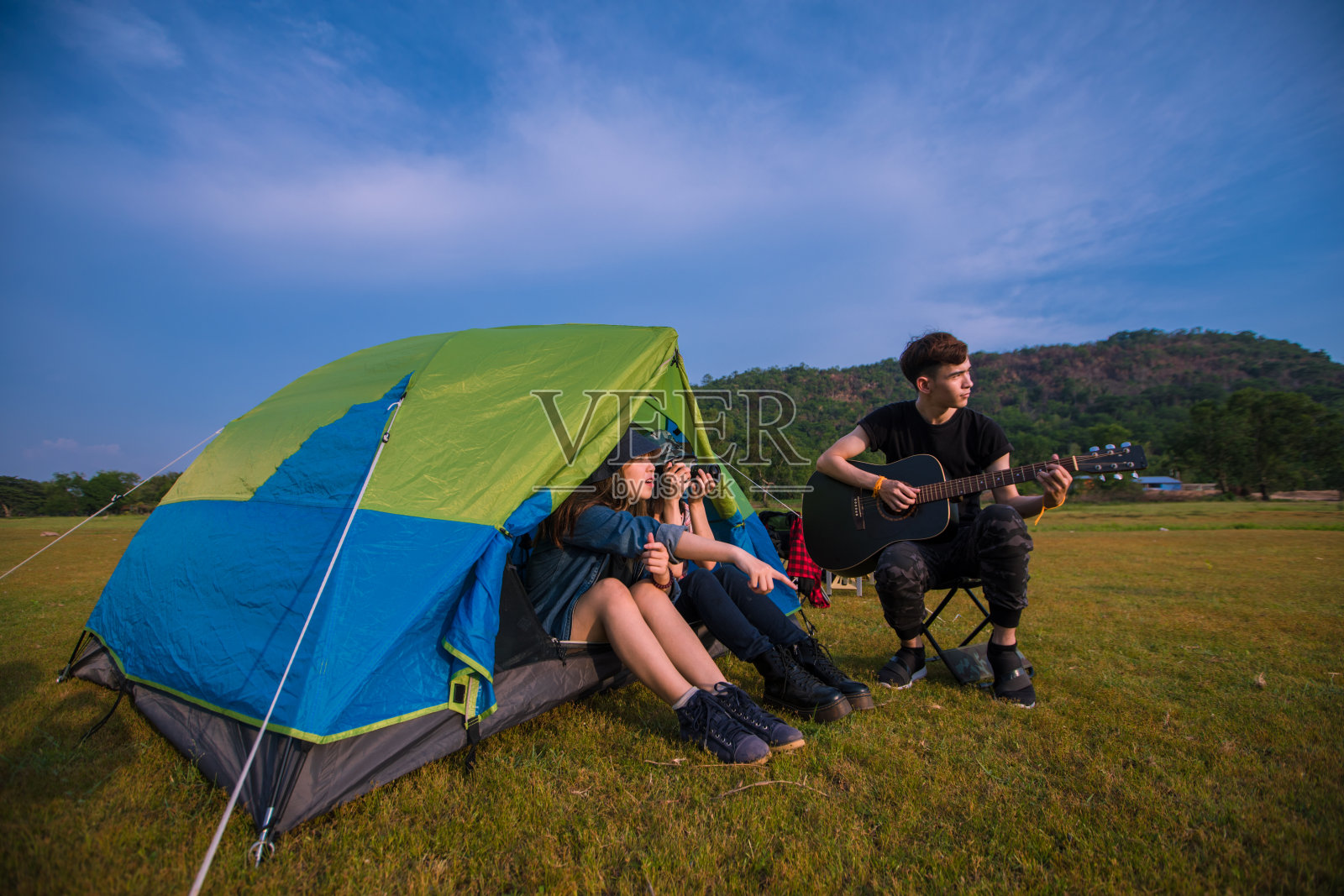 一群亚洲朋友在夏天一起喝酒和弹吉他，在日落时分在湖边露营照片摄影图片