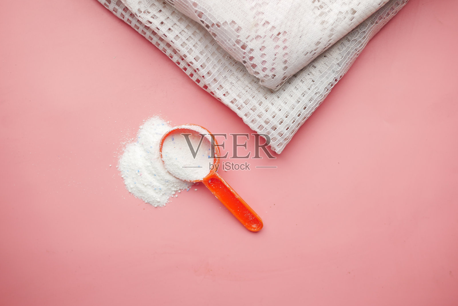 粉红色背景上的塑料勺里的洗衣粉照片摄影图片