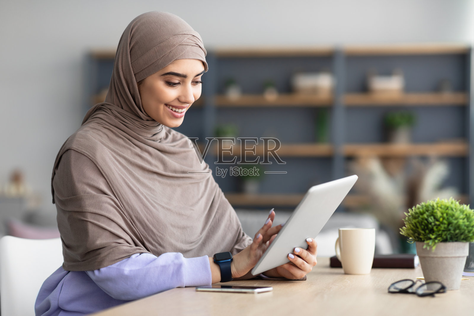 微笑的穆斯林妇女使用平板电脑坐在桌子上照片摄影图片