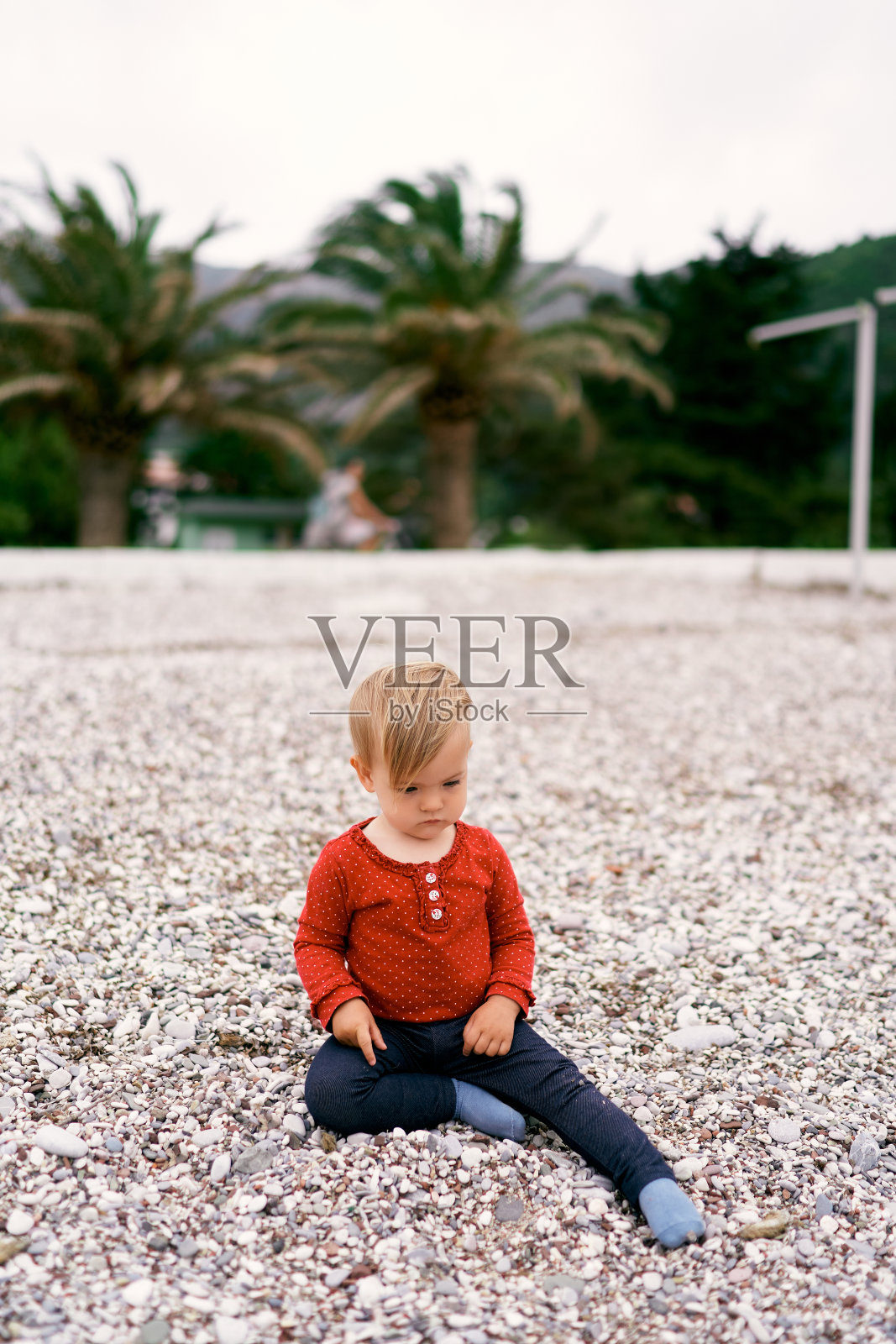 一个严肃的小孩坐在卵石滩上，背靠棕榈树照片摄影图片