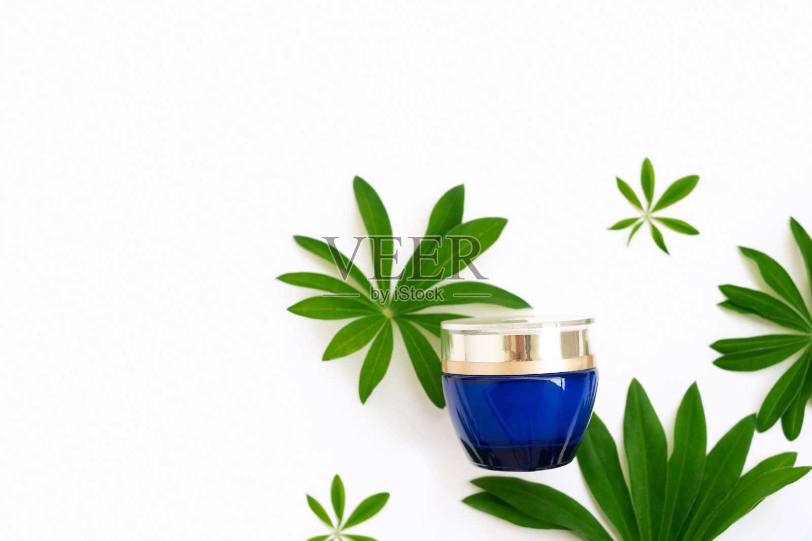 一个蓝色的瓶子，上面有保湿抗老化的霜，白色的背景上有绿色的羽扇豆叶子。平的。模型照片摄影图片
