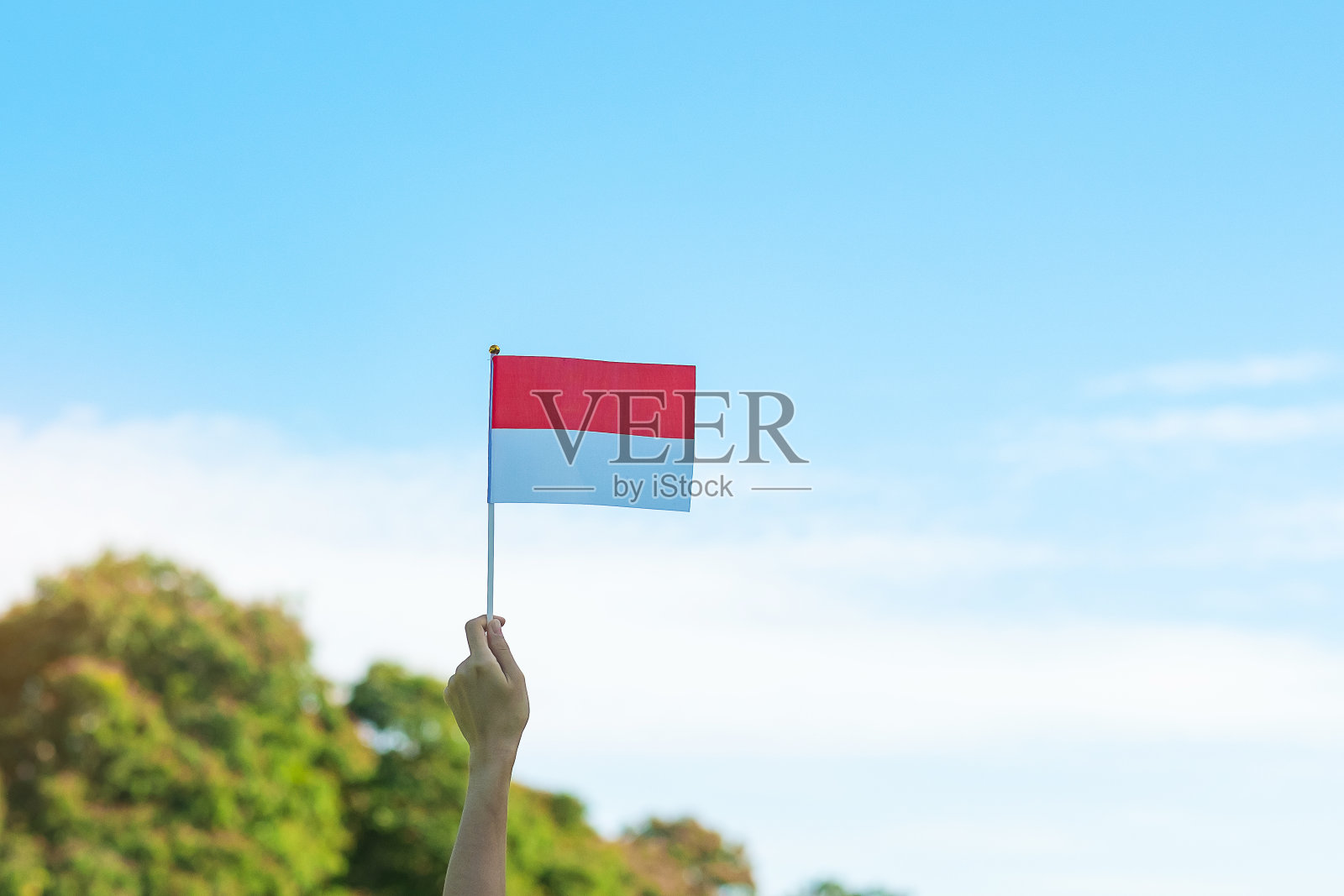 在蓝天的背景下，手握印尼国旗。印度尼西亚独立日、国庆日和快乐庆祝概念照片摄影图片