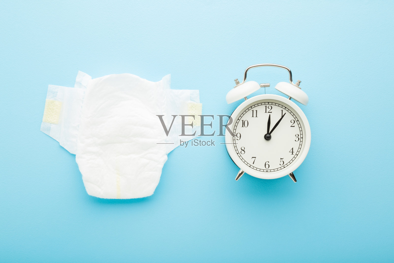 闹钟和白色柔软的婴儿尿布在浅蓝色的桌子背景。柔和的颜色。特写镜头。尿布改变了时间观念。自顶向下的观点。照片摄影图片