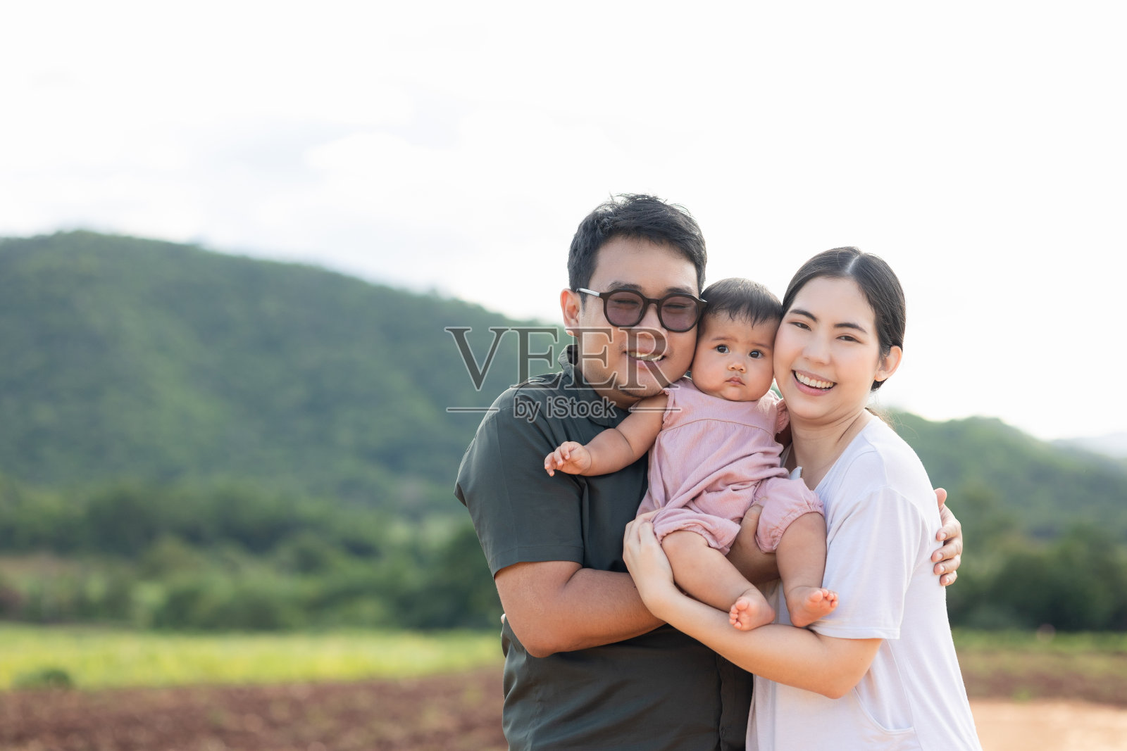 幸福的亚洲家庭父亲母亲孩子女儿的自然背景。阳光明媚的日子里，父母抱着小宝宝站在户外。照片摄影图片