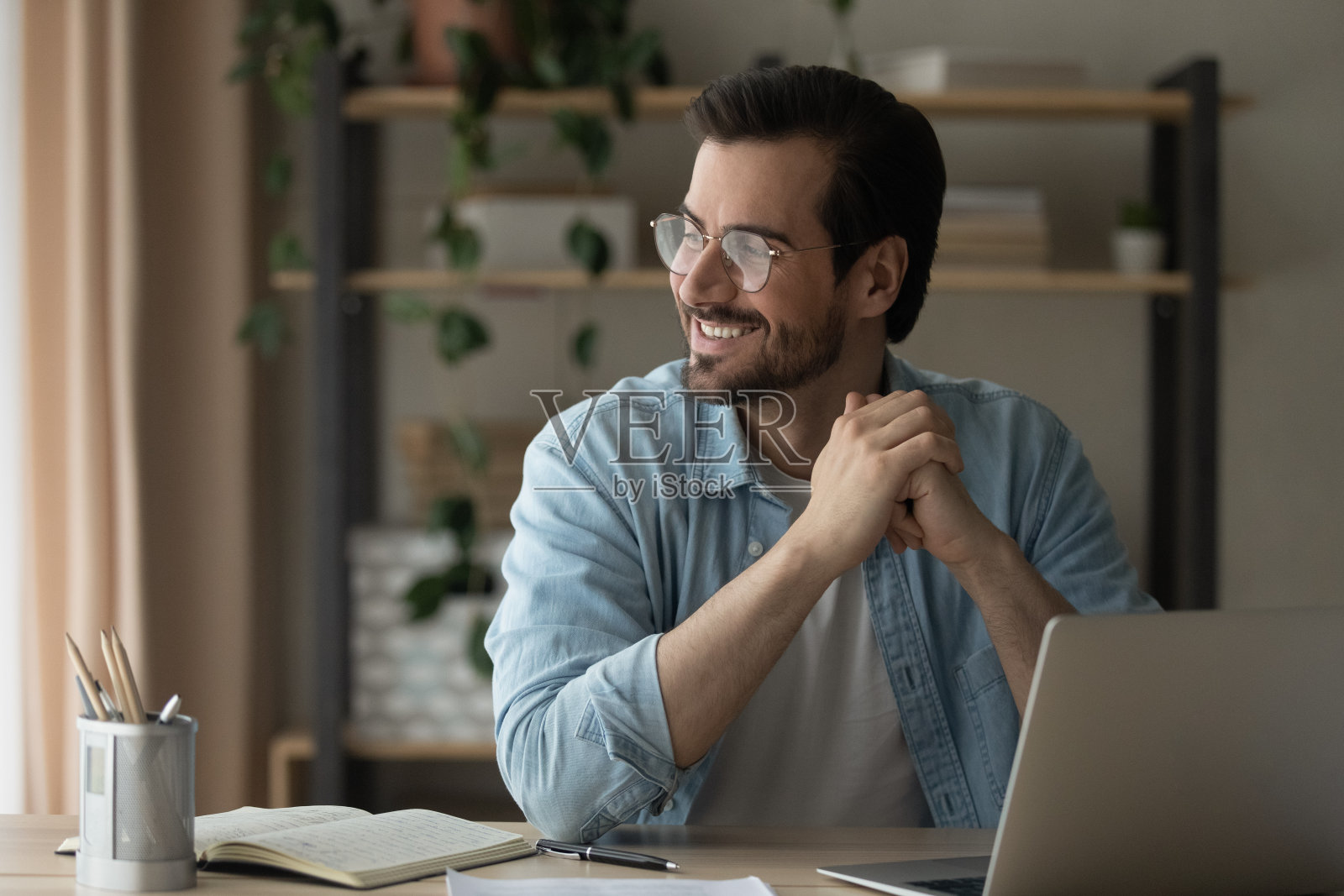 戴着眼镜，面带微笑的年轻人从电脑工作中分心。照片摄影图片