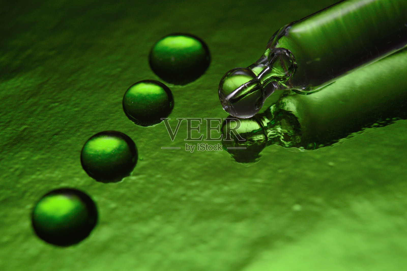 一个化妆用的液体移液管放在绿色的背景上，上面覆盖着液滴。特写镜头。照片摄影图片