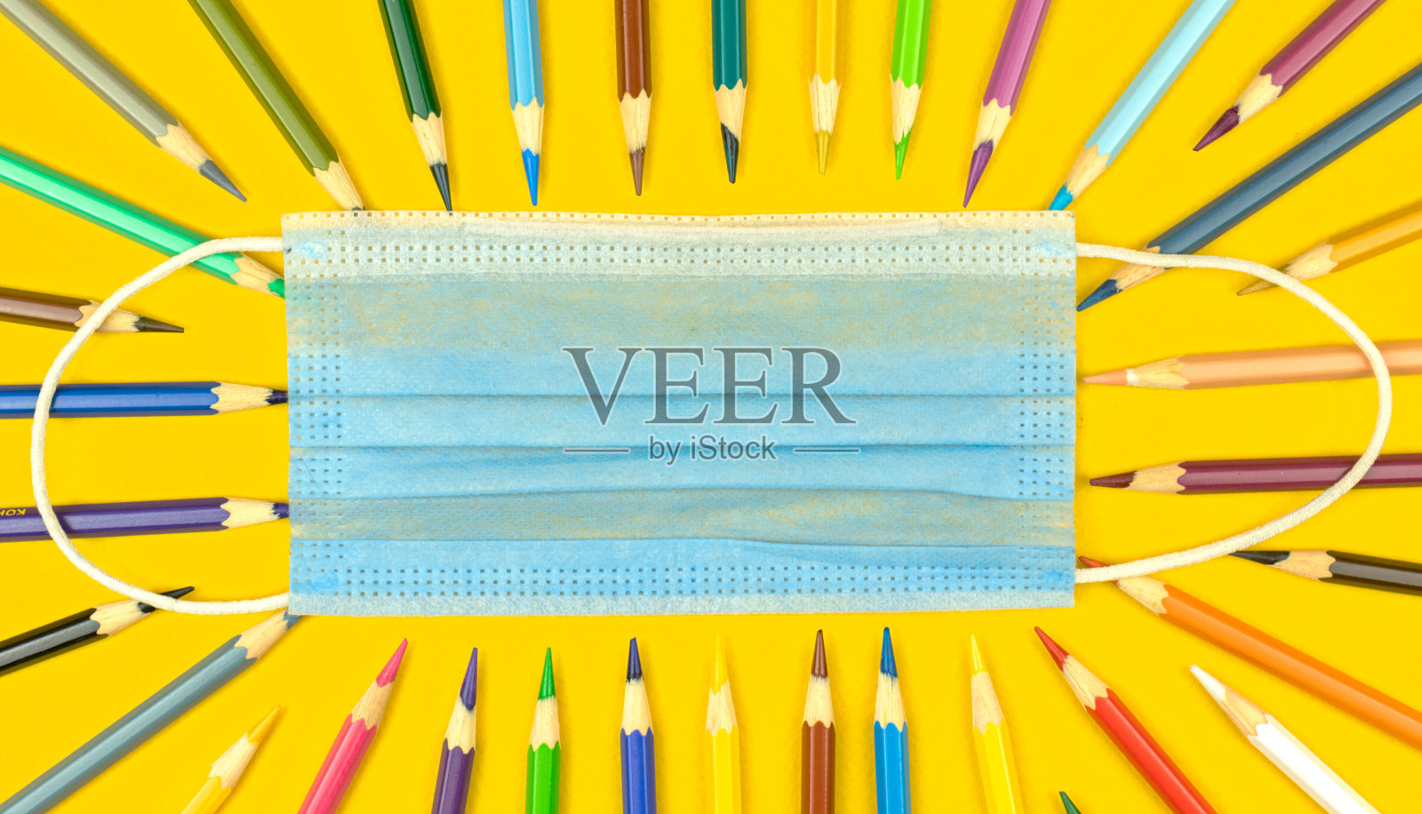 返校期间，带医用口罩进行概念教育，黄色桌面上彩色铅笔，俯视图照片照片摄影图片