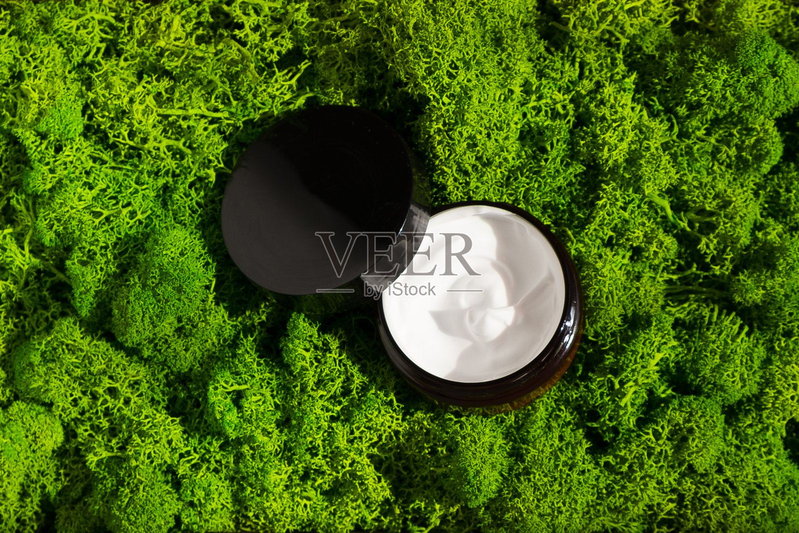 在晨光的照射下，在青苔背景上的一瓶美容霜。有机粘土面膜霜适用于脸部和身体。护肤美容概念，水疗养生中心，面部护理照片摄影图片