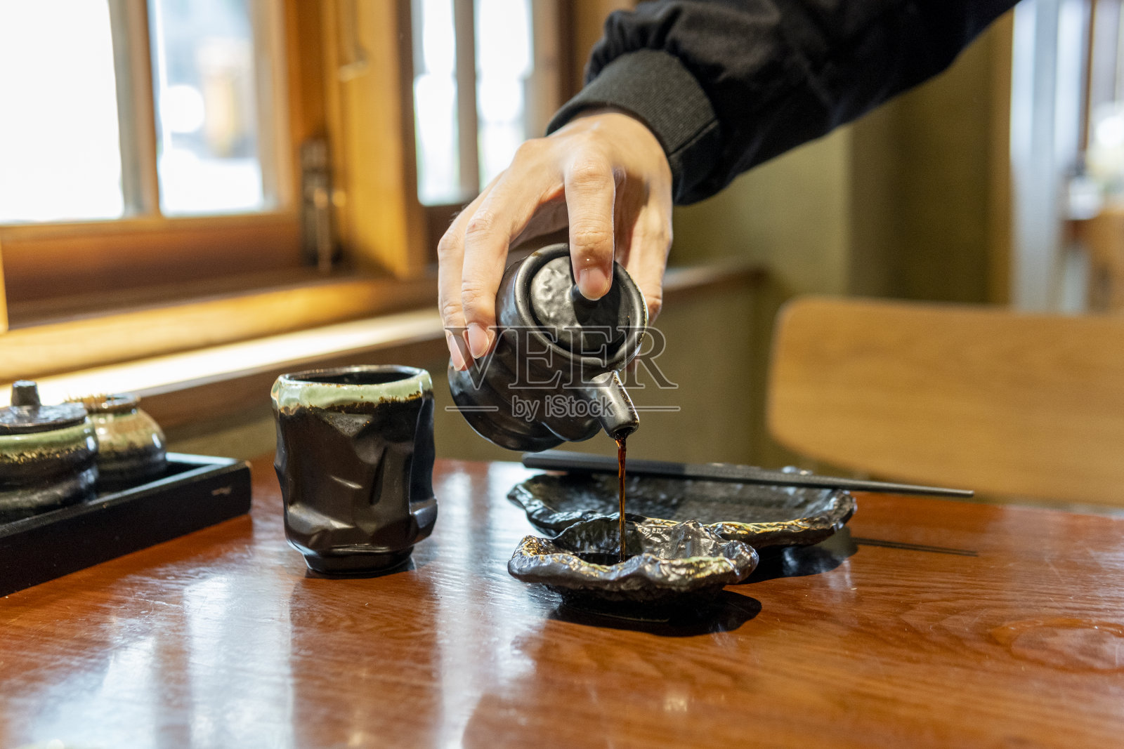 在日本餐馆里，把酱油倒进碟子里的手照片摄影图片