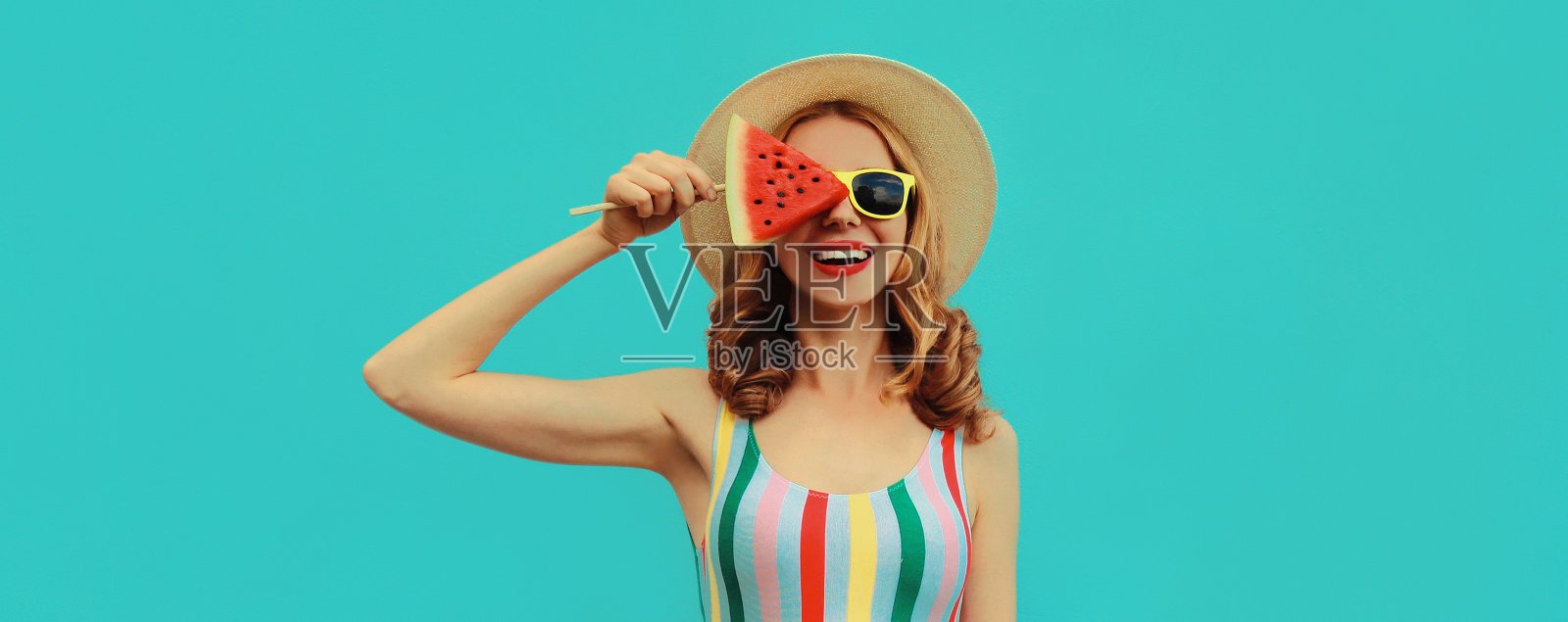一个快乐微笑的年轻女子的夏天肖像与棒棒糖或冰淇淋形状的西瓜片戴着草帽在一个蓝色的背景照片摄影图片