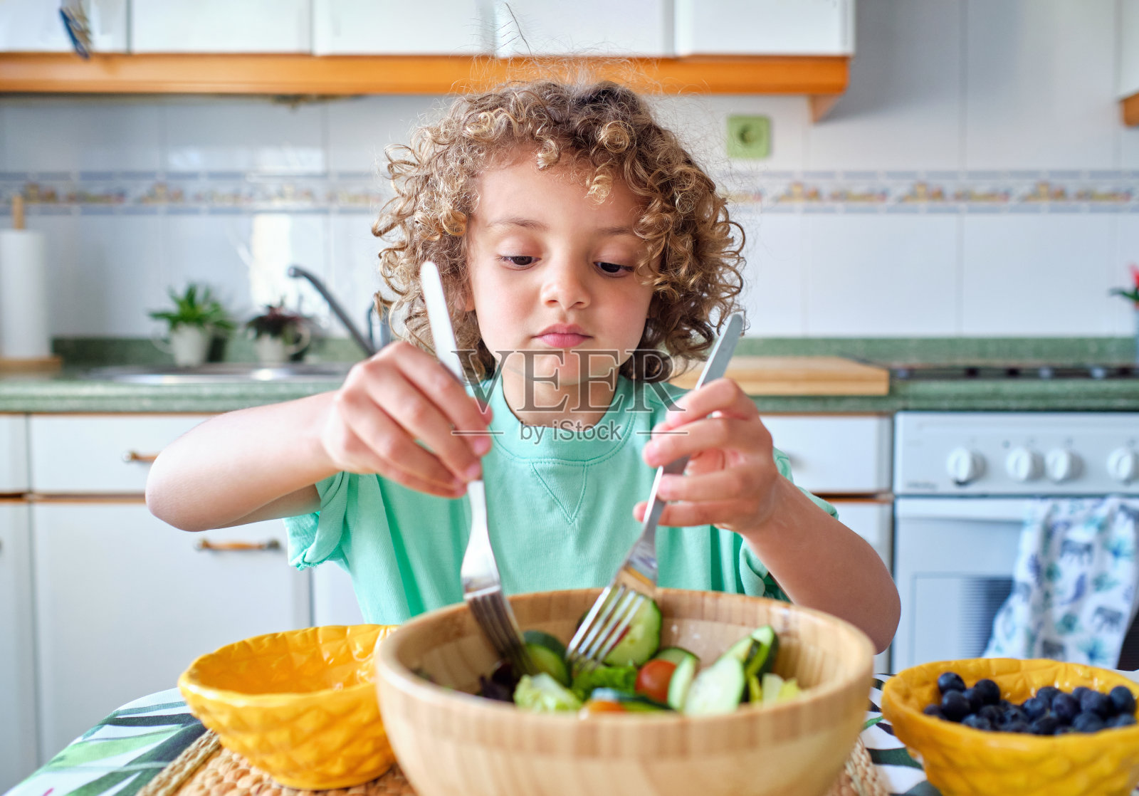 西班牙儿童在家庭厨房里混合健康的素食沙拉照片摄影图片